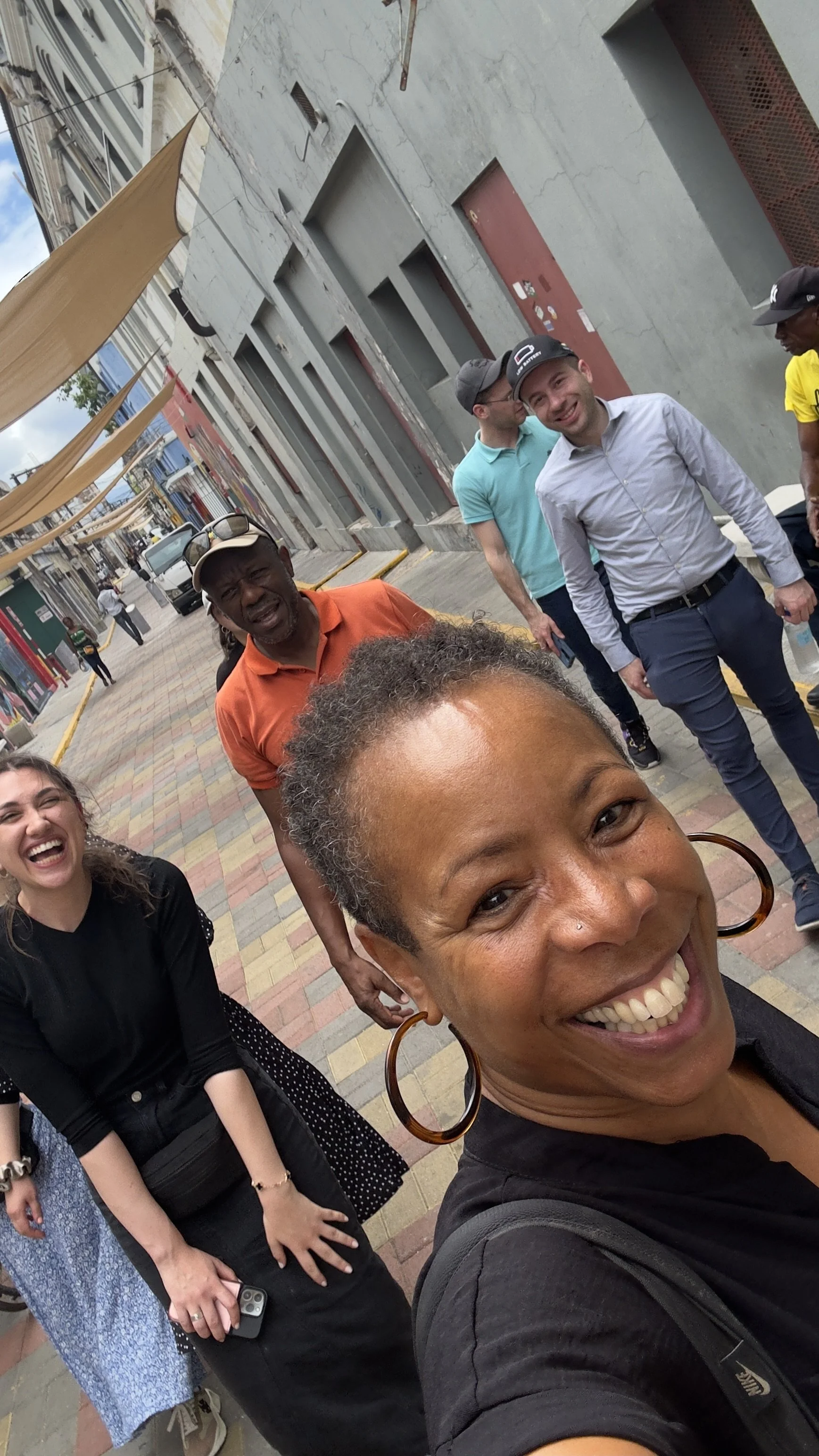 A group of diverse people smiling and laughing on a colorful outdoor city street downtown Kingston, Jamaica, taking a selfie.