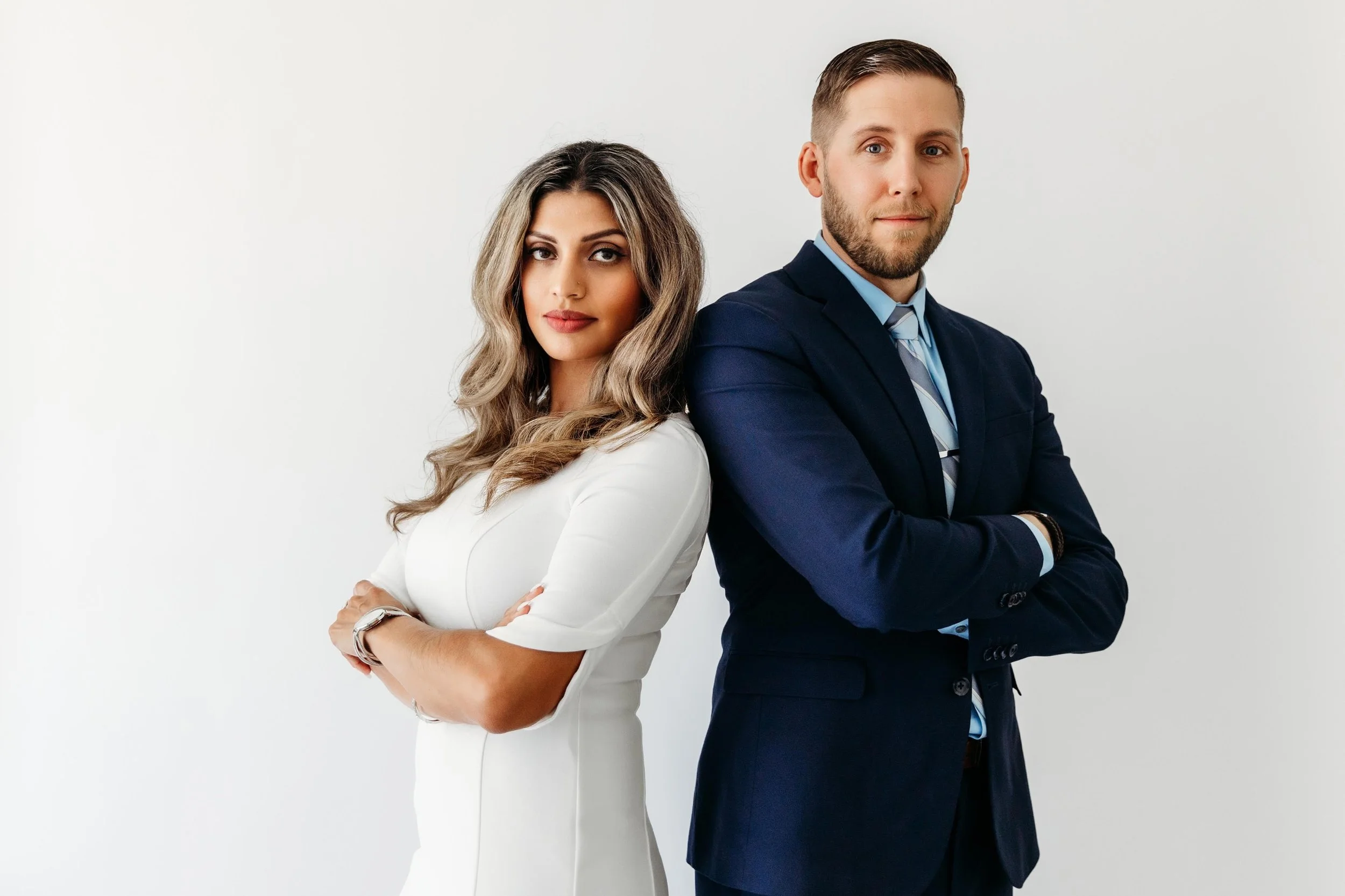 Professional woman and man standing back to back with arms crossed, wearing formal business attire against a white background.