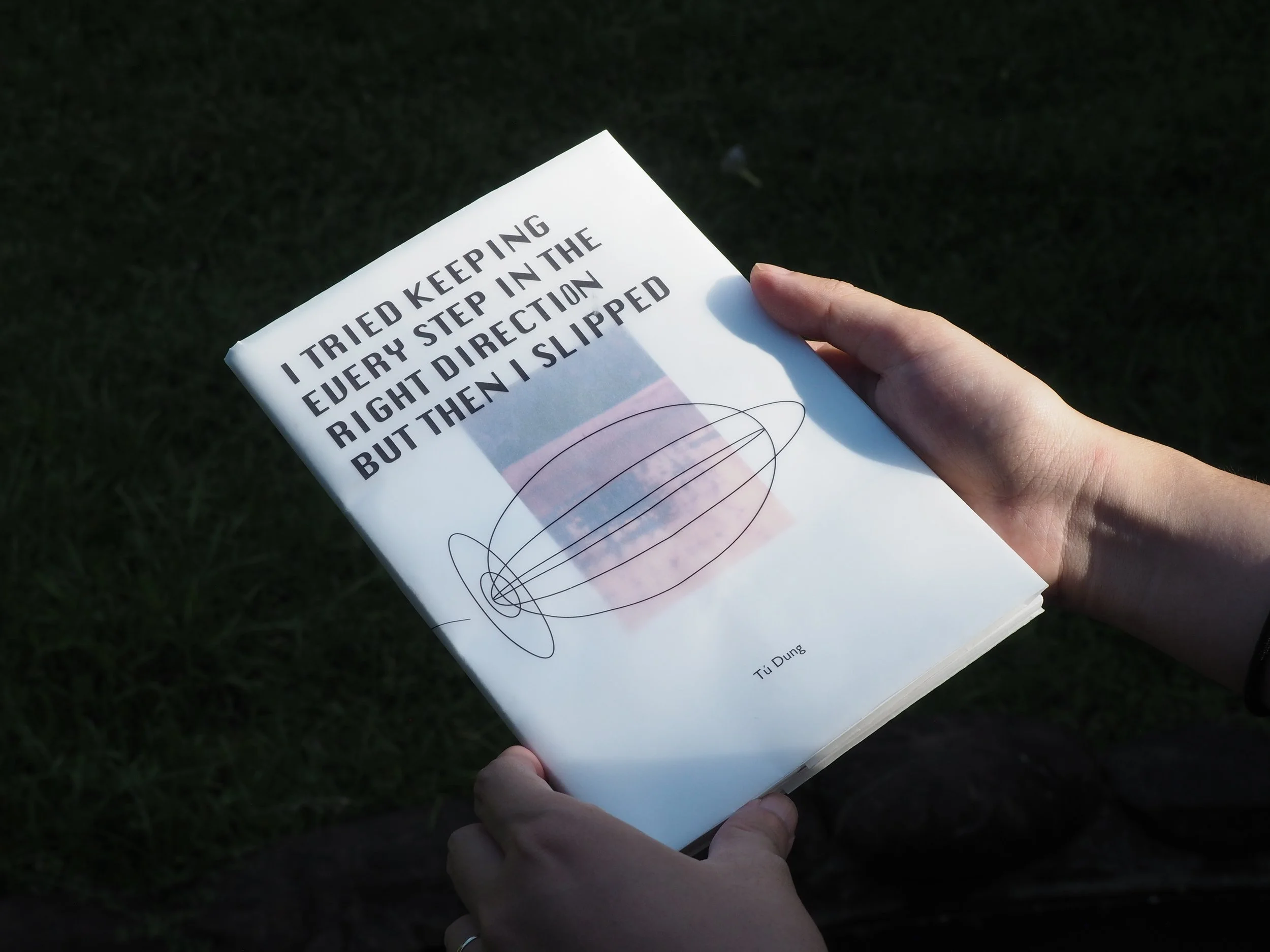 Book titled 'I Tried Keeping Every Step in the Right Direction But Then I Slipped' held in person's hands outdoors with green grass background.