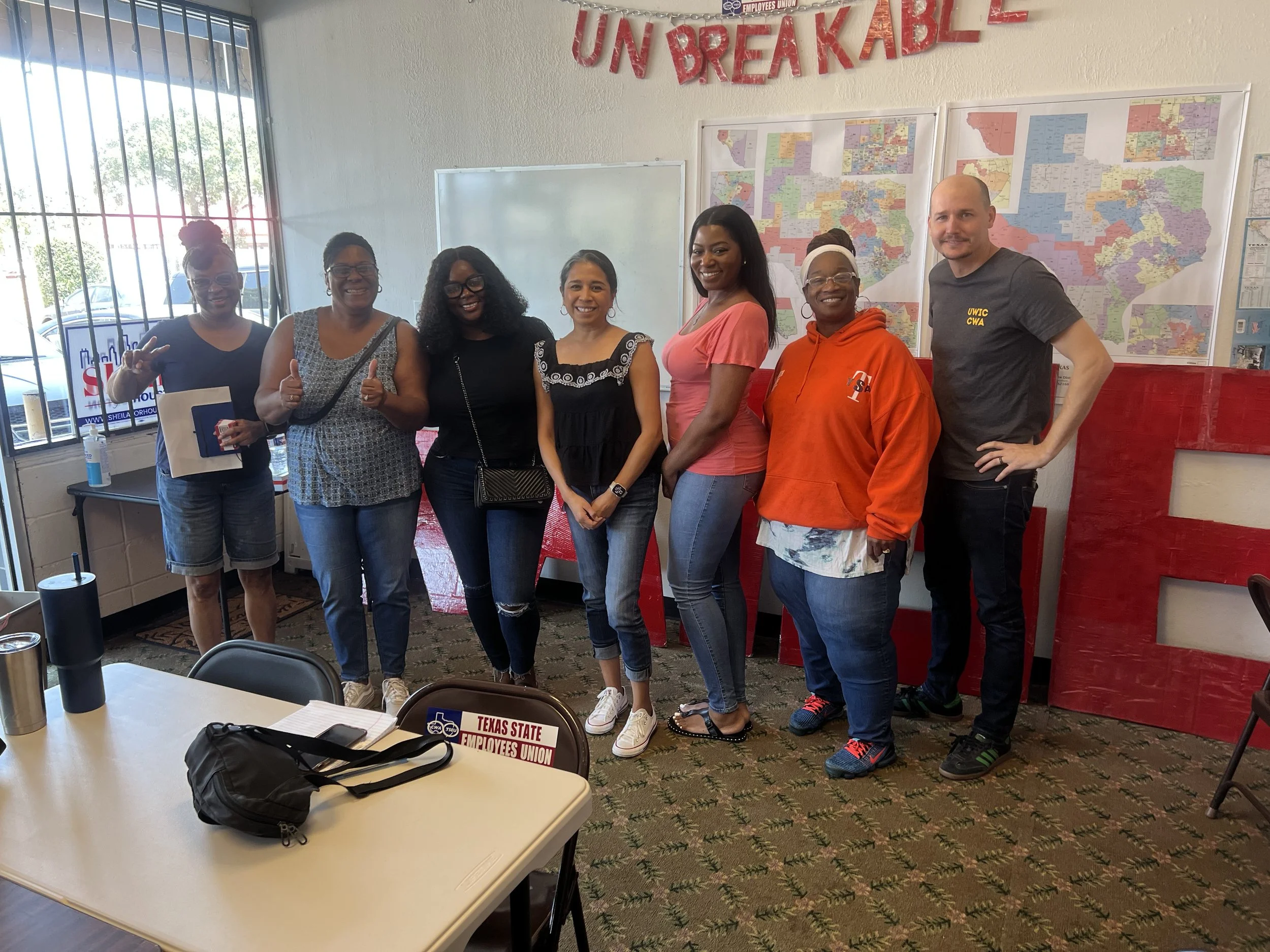 A group of seven smiling people, posing together under a red glitter sign that says "unbreakable"