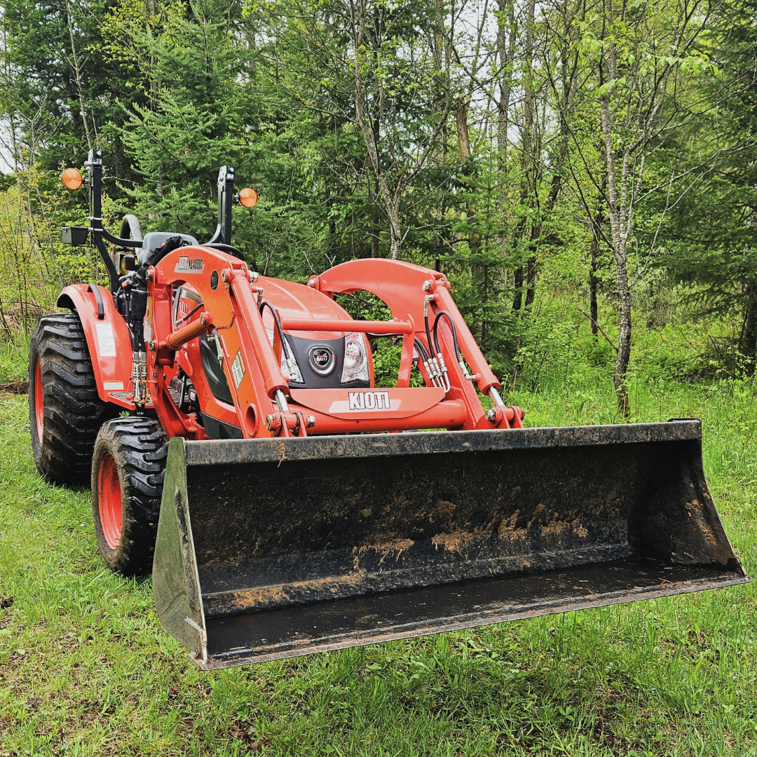 Image of an orange tractor with grass and trees in the background.