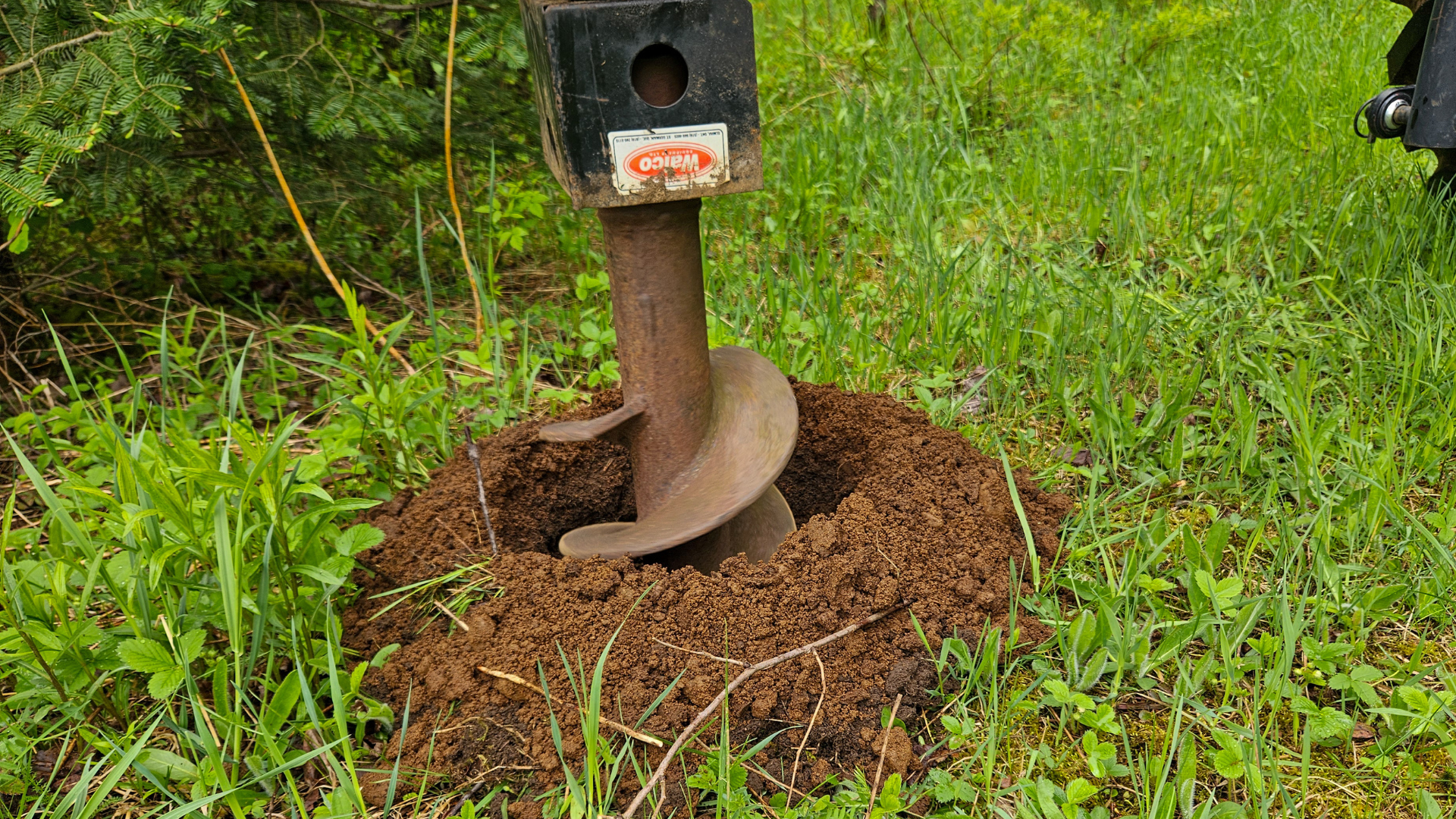 Picture of a tractor-mounted auger drilling a hole in the grass.