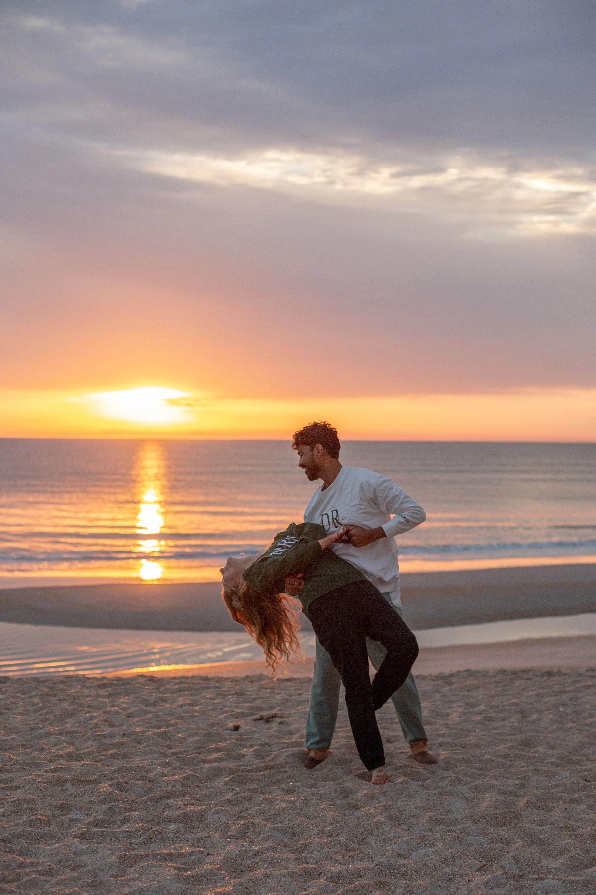 Interracial wedding photography. Young couple before their wedding day during sunrise on the beach, man is dipping wife as they were dancing. 