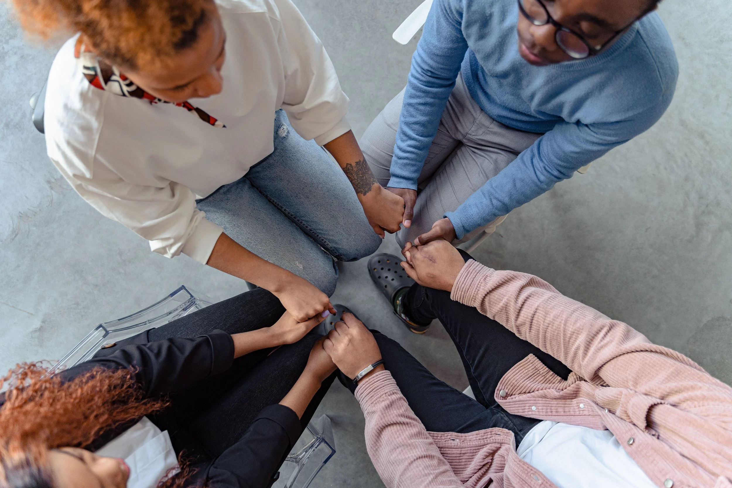Group of diverse people sitting in a circle holding hands in the center, symbolizing unity and teamwork.