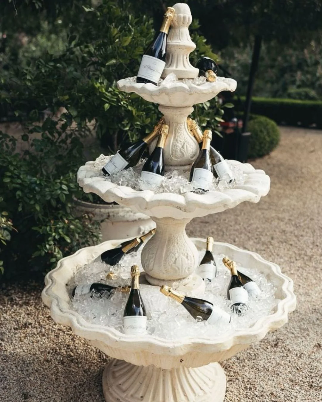 Tiered stone fountain filled with ice and champagne bottles at an elegant outdoor Italian wedding reception.