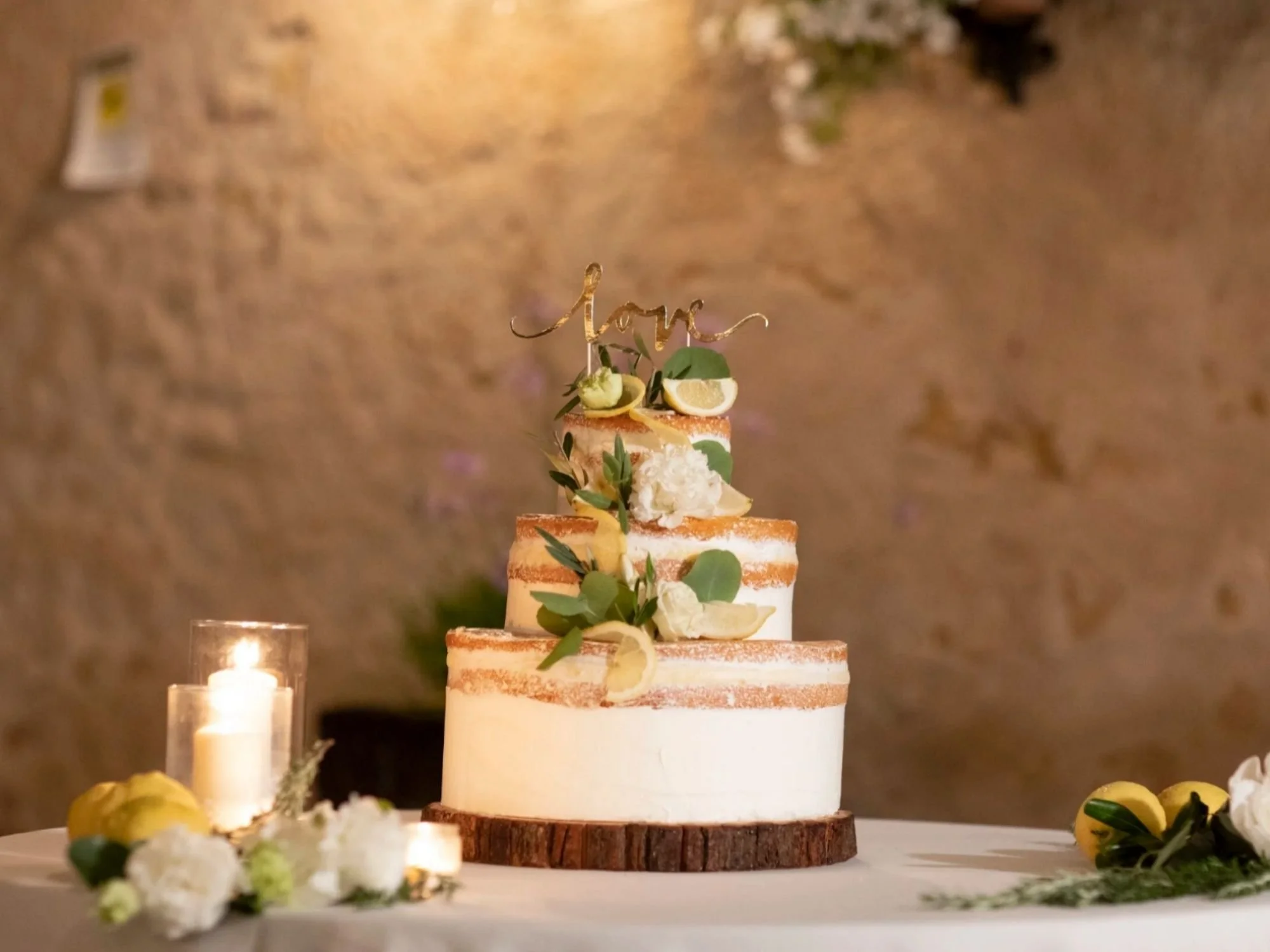 A three-tiered naked cake adorned with lemons and greenery, glowing beside soft candlelight at a Sicilian wedding.