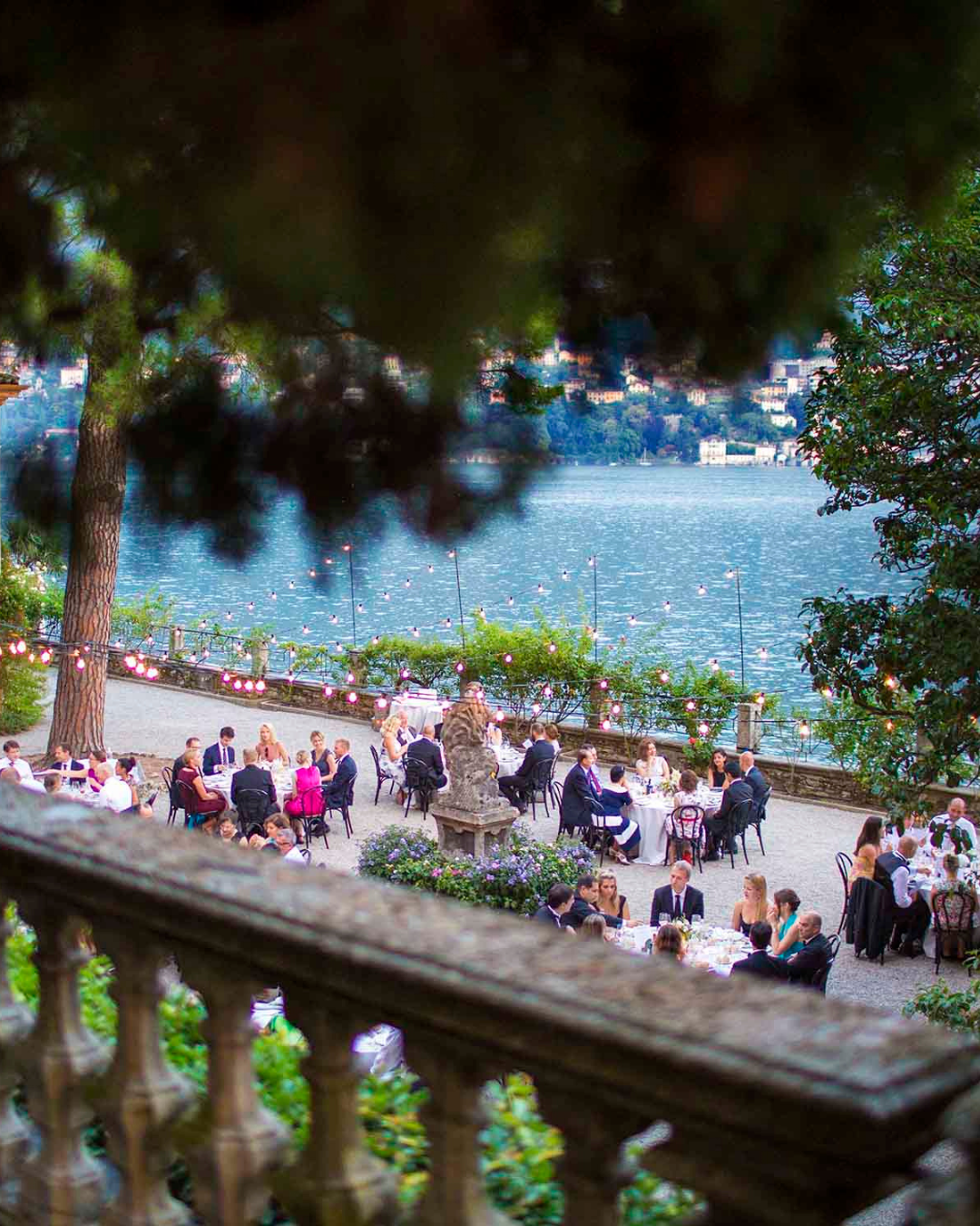 Outdoor wedding reception by Lake Como with guests dining under string lights overlooking the water and mountains in Italy