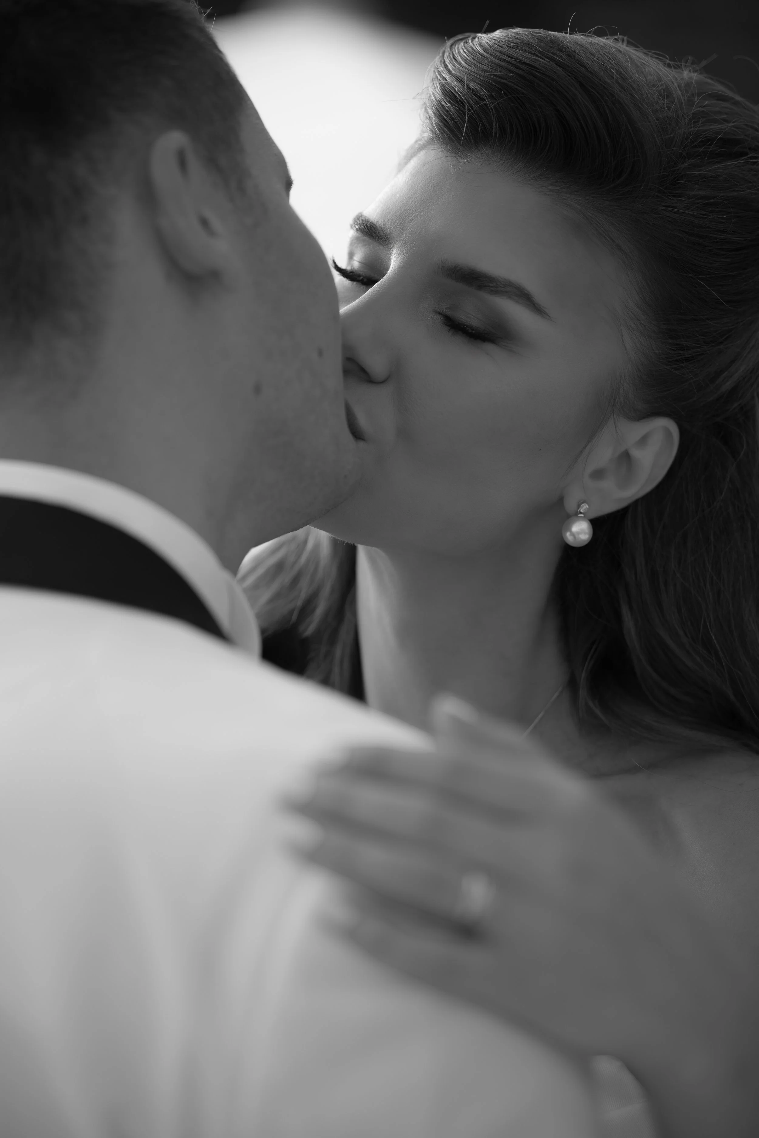 Close-up black and white portrait of a bride and groom sharing a kiss during their wedding day.