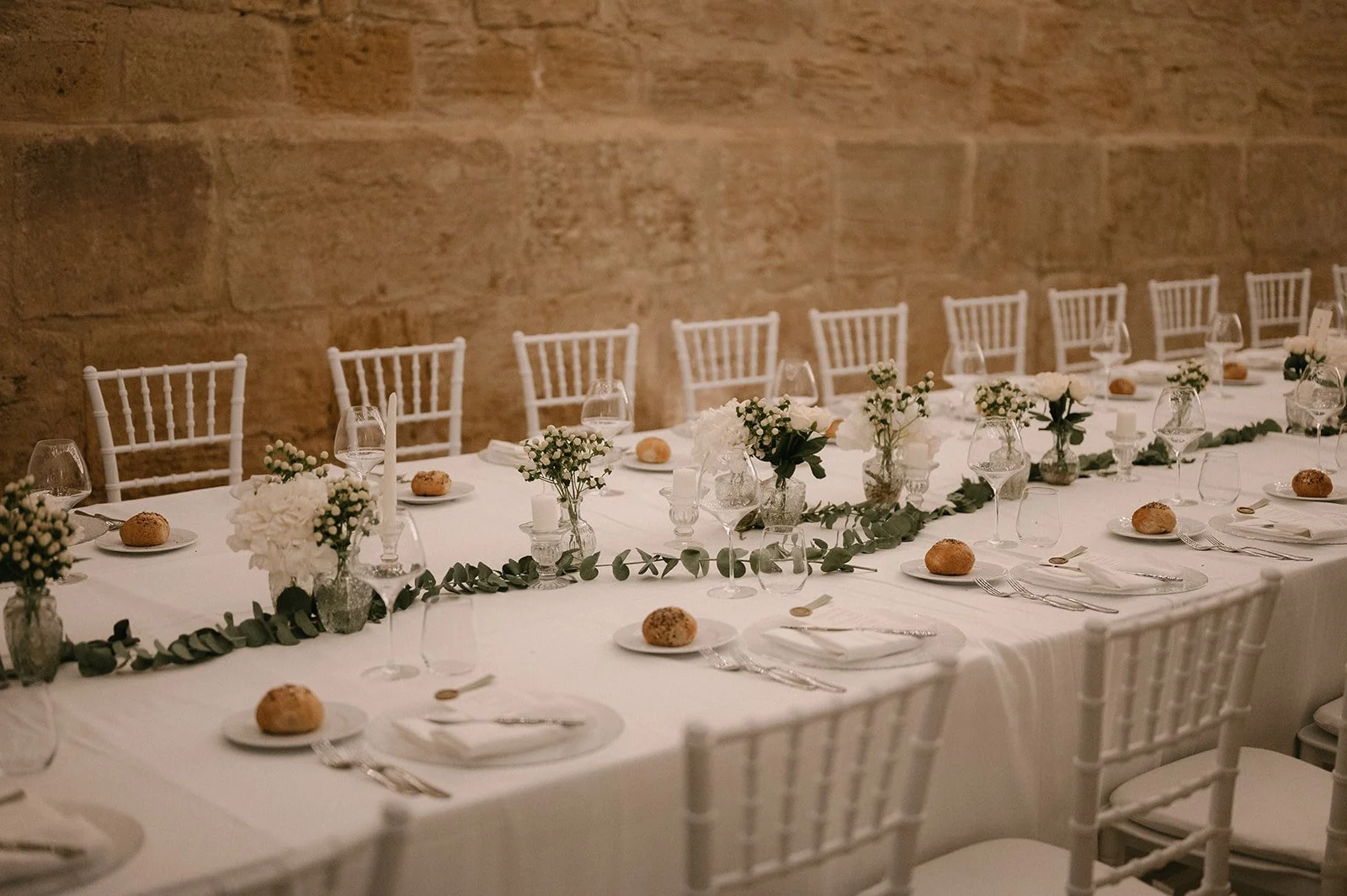 Elegant white wedding reception table in Sicily with soft floral arrangements, eucalyptus, candles, and timeless styling by Alla Flora Giapponese.