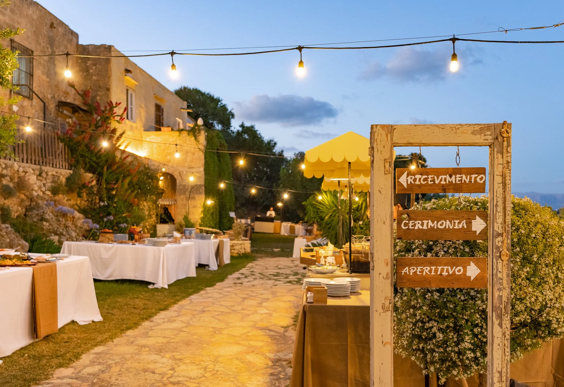 Rustic Italian wedding reception courtyard at dusk with fairy lights, outdoor dining tables, and romantic ambiance.