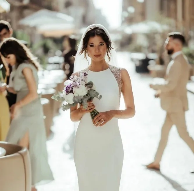 Bride walking through an Italian wedding venue holding a white and purple bouquet in soft golden light.