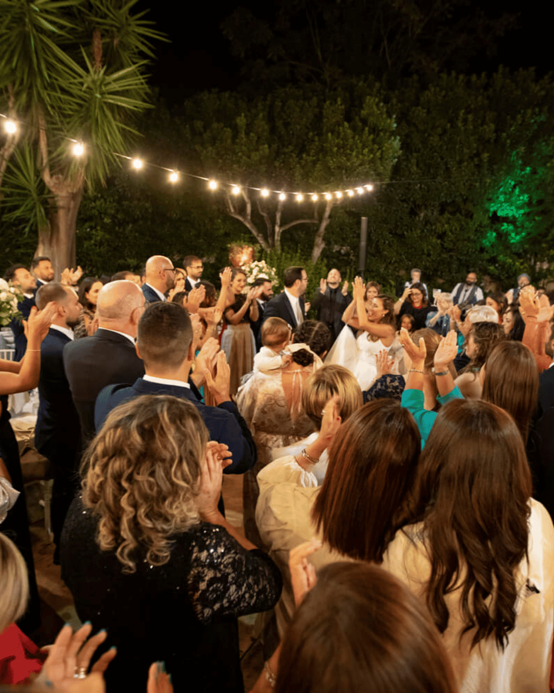 Wedding guests celebrating outdoors at an Italian wedding reception in Sicily, gathered beneath festoon lights as the newlyweds dance among family and friends.