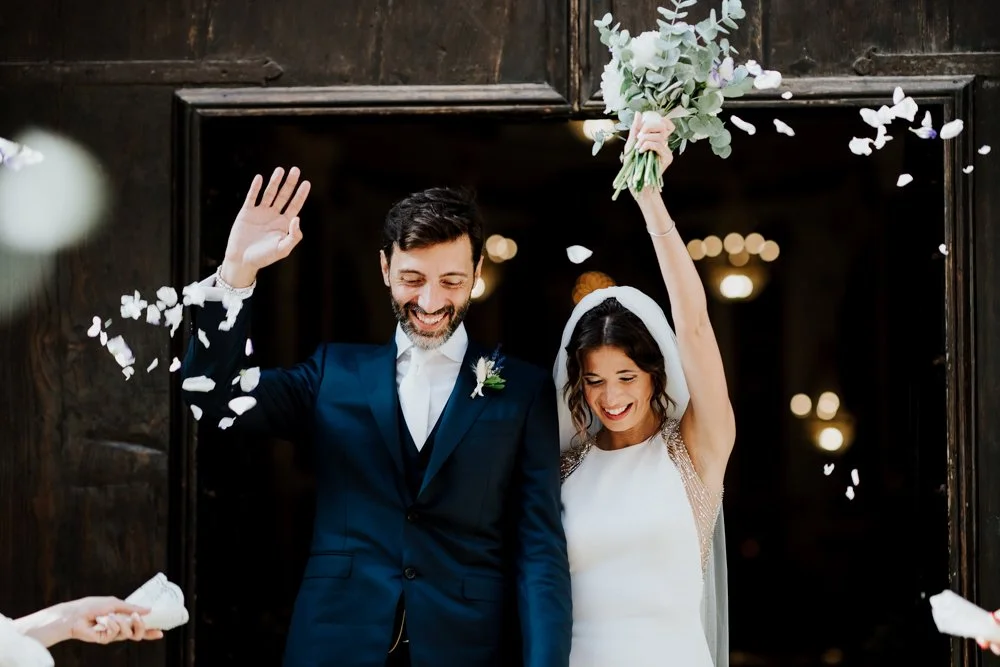 Bride and groom celebrating outside a Sicilian church entrance with flower petals, joyful smiles, and an elegant bridal bouquet during their Italy wedding celebration.