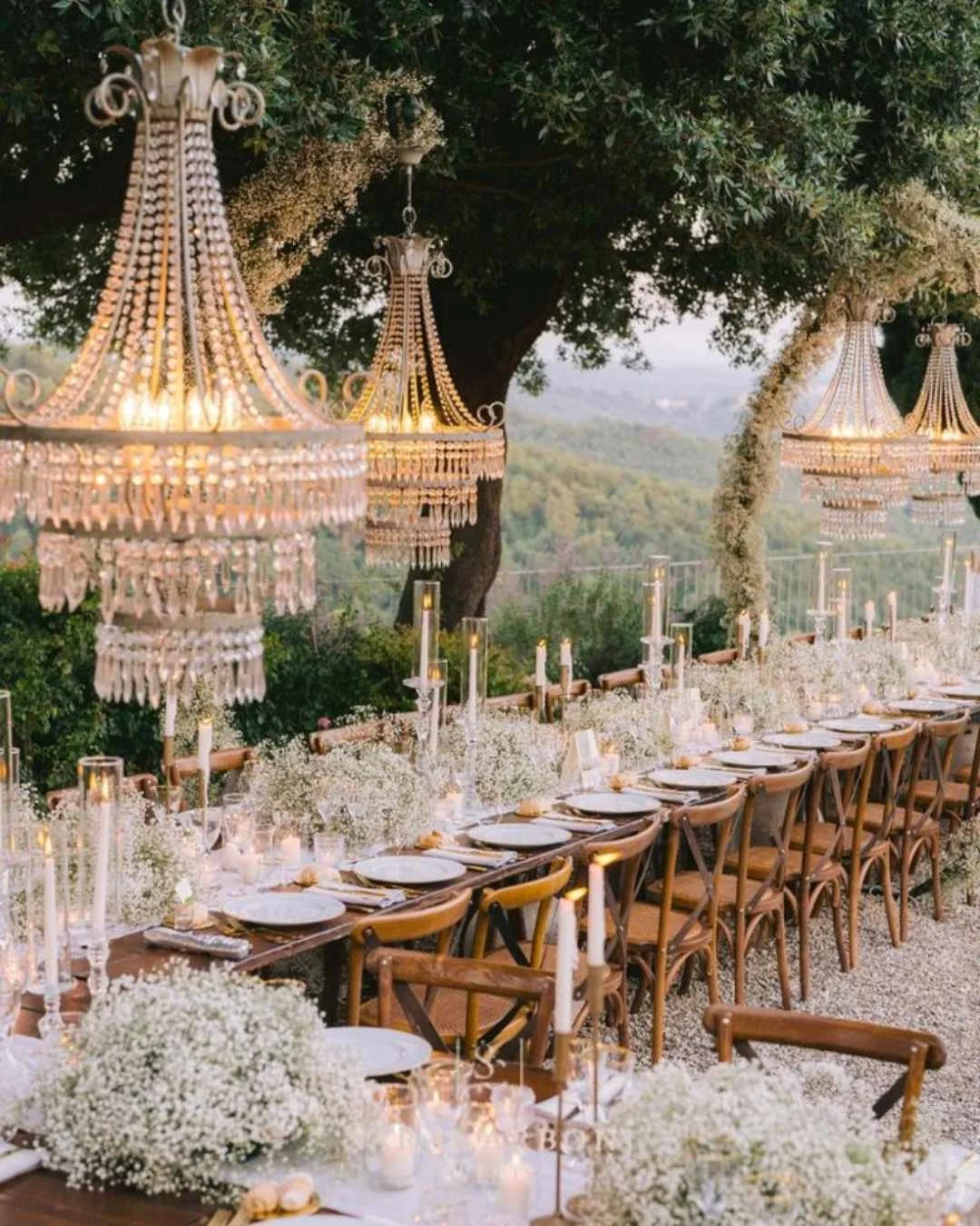 Romantic long-table dinner under crystal chandeliers in an Italian garden at sunset, with candlelit florals.
