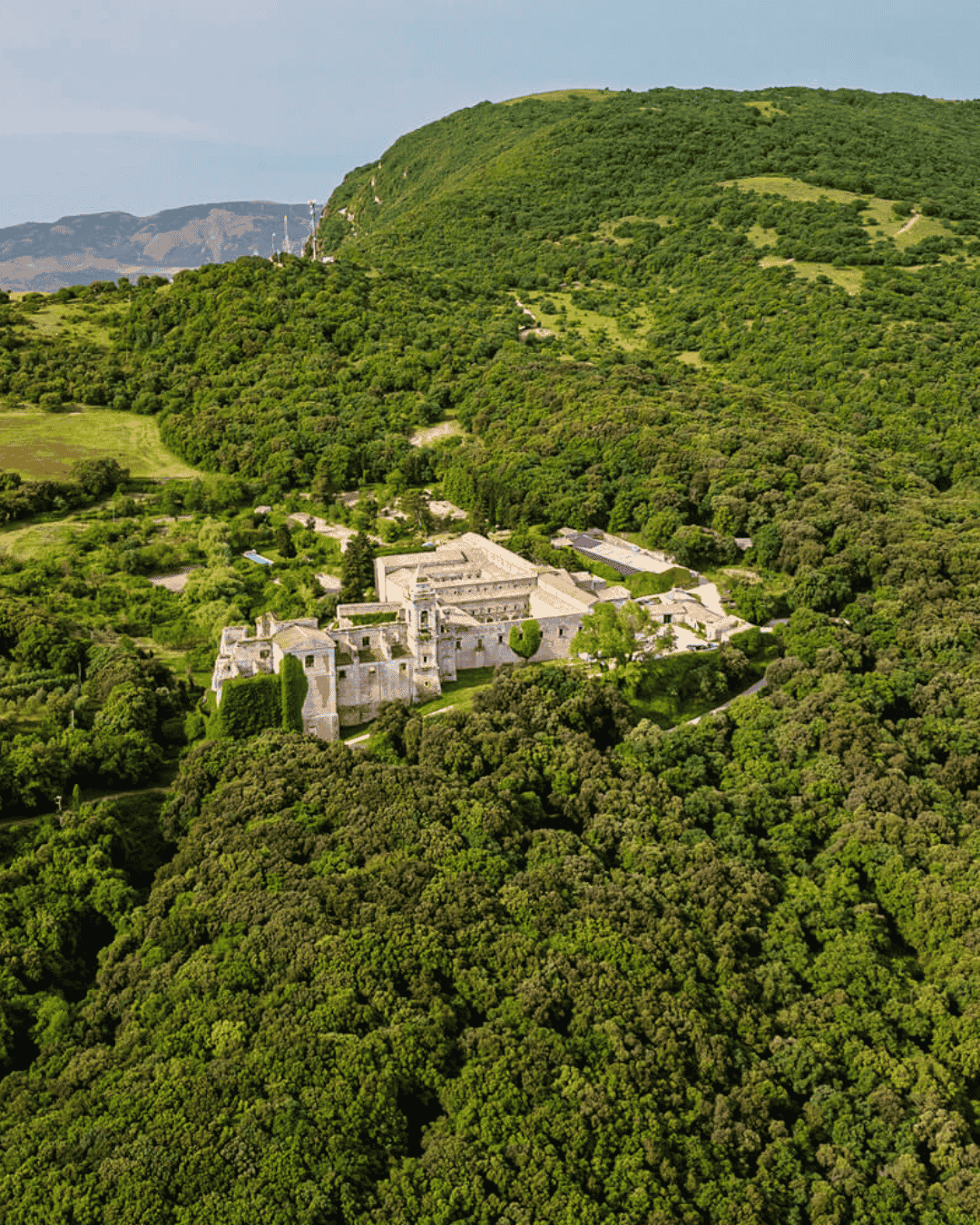 Aerial view of a historic Sicilian wedding venue surrounded by rolling green hills and woodland, showcasing the secluded beauty of the Italian countryside.