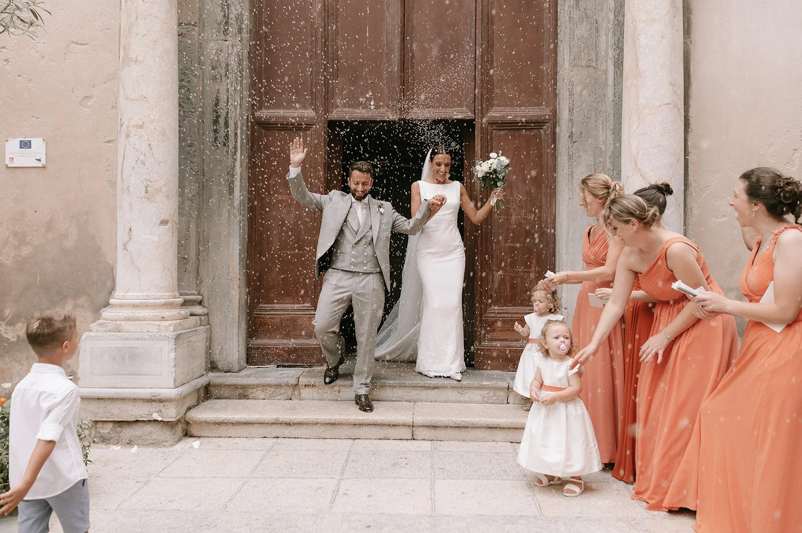 Bride and groom celebrating outside an Italian church during their wedding exit surrounded by guests and confetti.