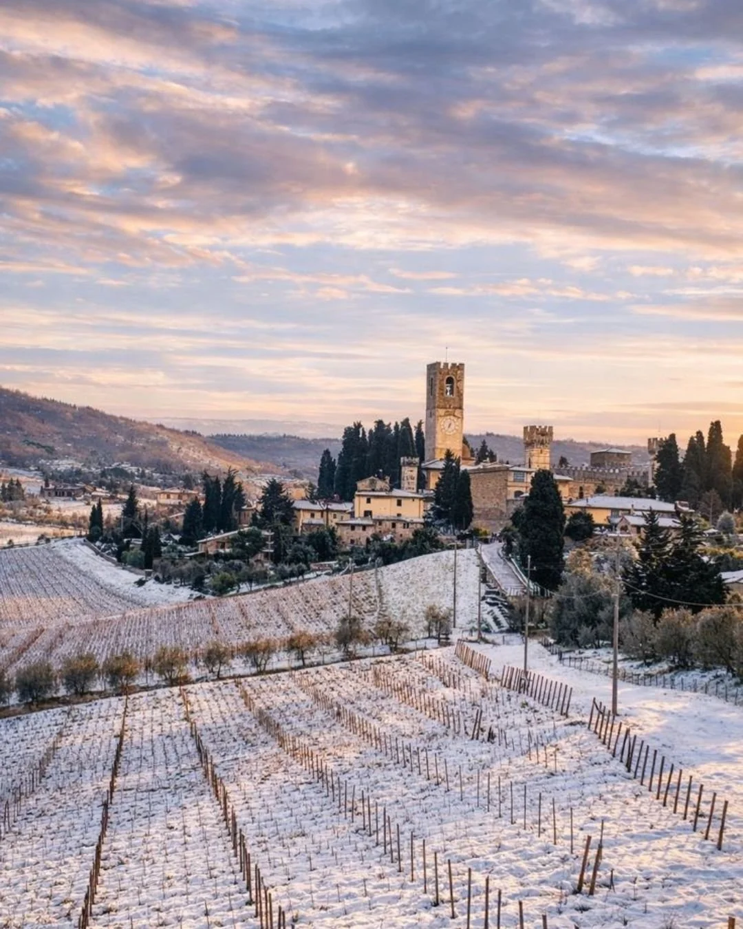 Winter landscape in Tuscany with frosted vineyards, rolling hills, and a historic village under a pastel sunset sky.