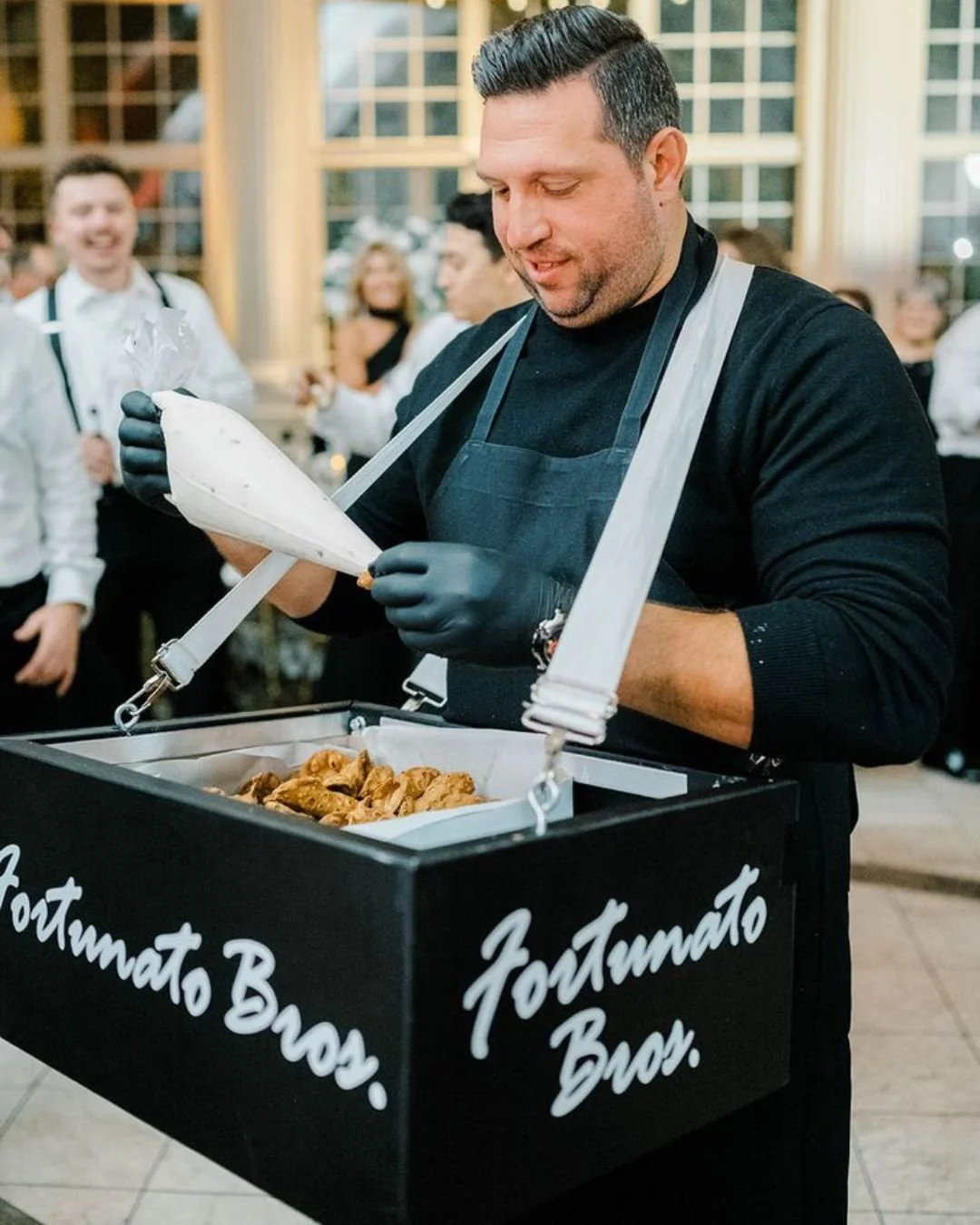 Live cannoli station at an Italian wedding reception with chef filling fresh cannoli for guests indoors.
