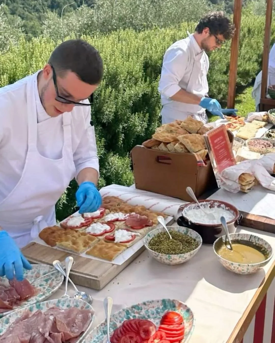 Live Italian wedding aperitivo station with chefs preparing fresh focaccia topped with ricotta, tomatoes, and prosciutto overlooking Tuscan countryside