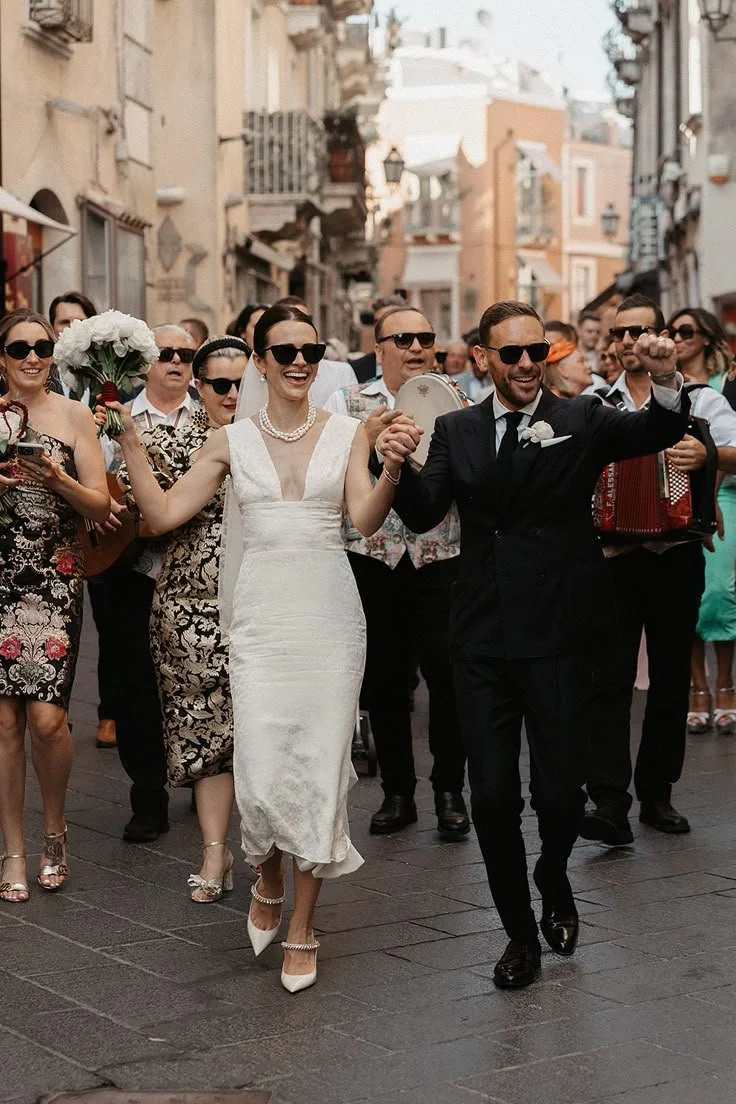 Bride and groom walking through Sicilian street wedding procession in Taormina with guests and live music