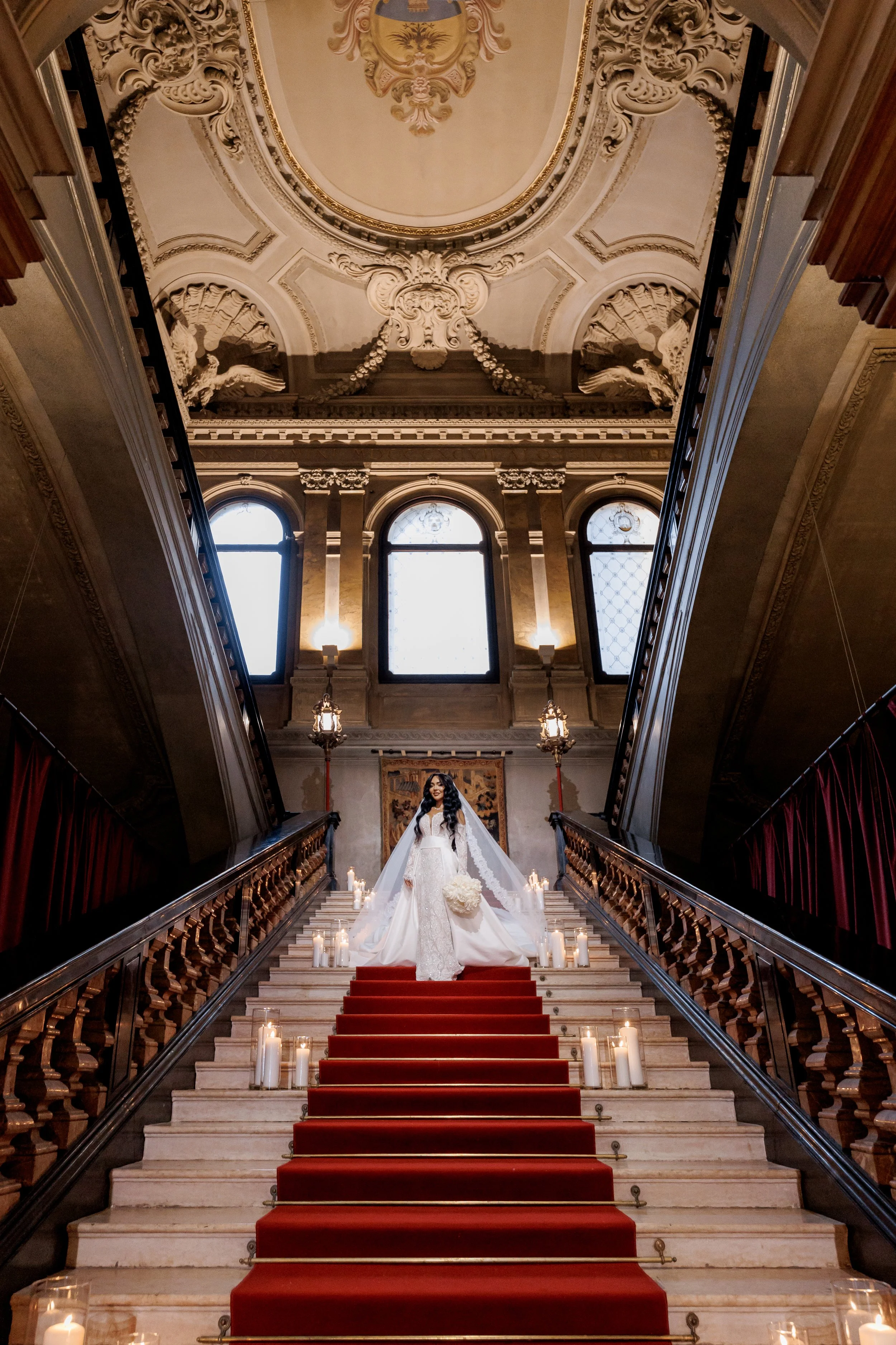 Bride standing on a grand staircase inside a historic Italian villa surrounded by candlelight and ornate architecture.