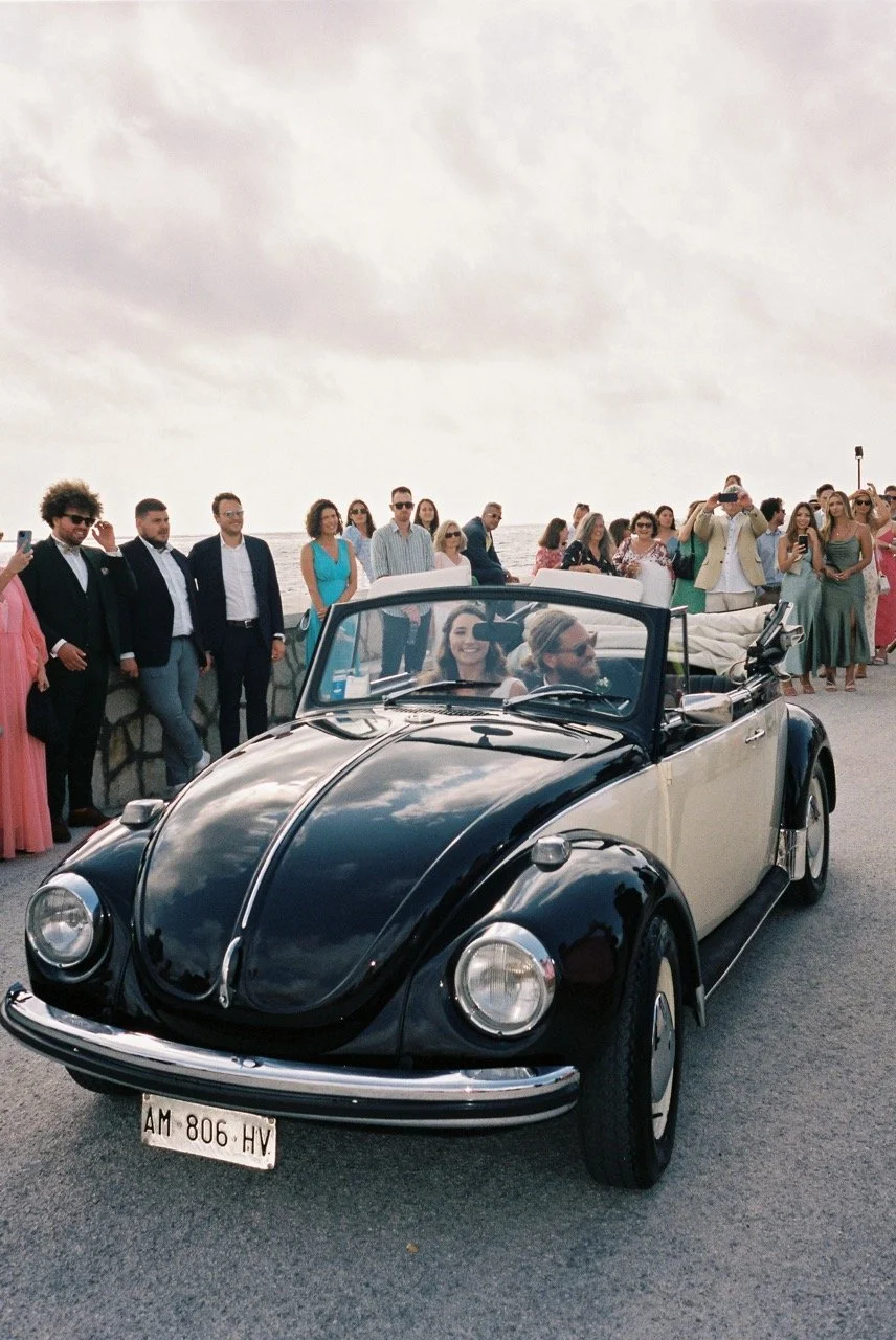 Newlyweds arriving in a vintage convertible Beetle beside the sea during their Italian wedding, photographed on film by Lauren Young.
