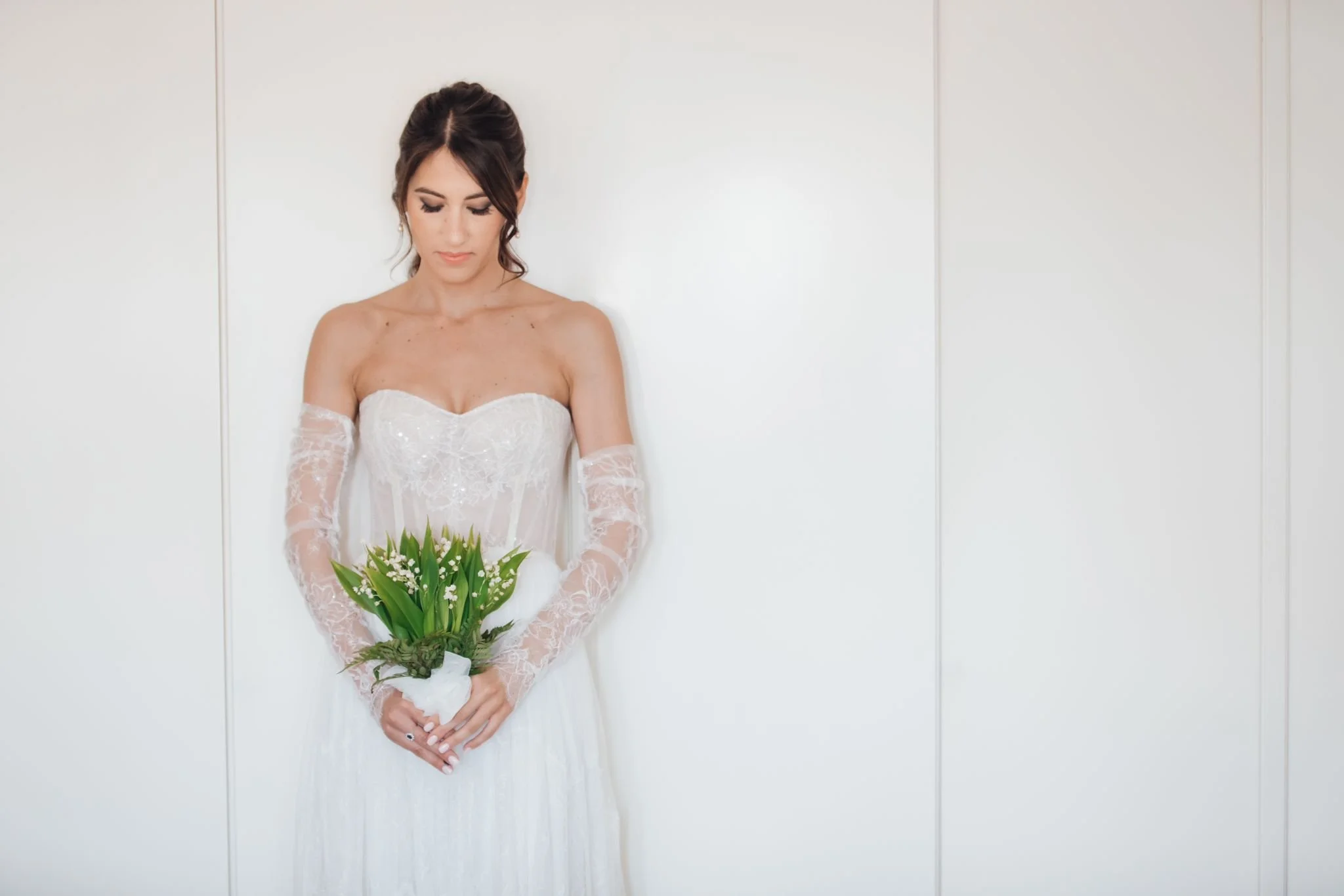 Elegant bride in a lace wedding gown holding a lily of the valley bouquet during a timeless Sicily wedding morning portrait.