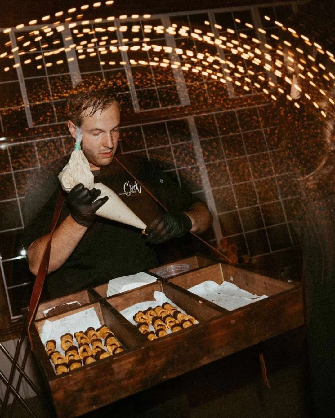 Chef piping fresh cannoli at a late-night Italian wedding party, capturing Sicilian flavours and guest interaction.