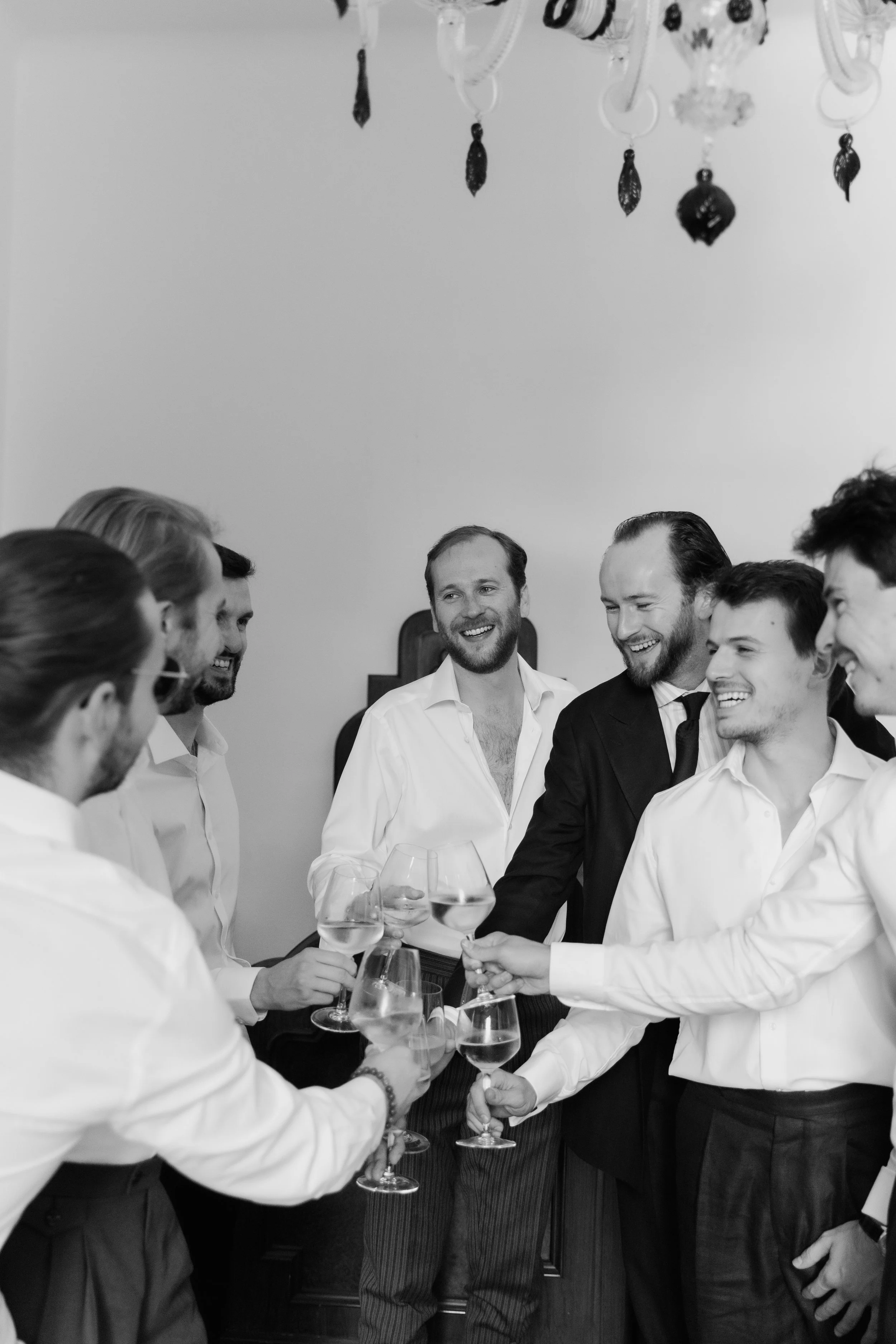Groom and groomsmen raising glasses while getting ready for an Italian wedding, photographed in black and white by Lauren Young.