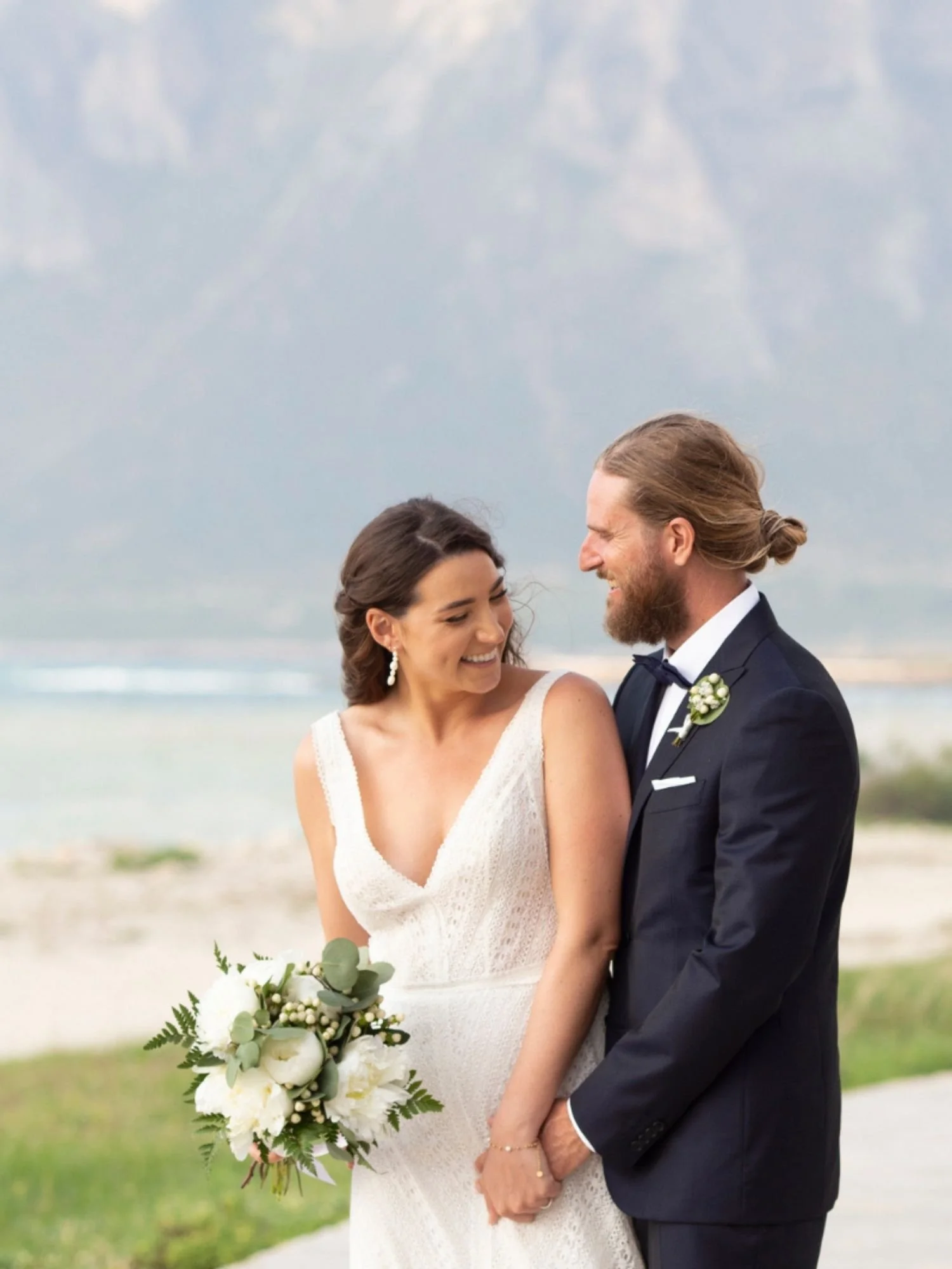 A candid seaside portrait of the bride and groom in Trapani, sharing laughter and joy with the mountains in the background — pure love and Sicilian magic.