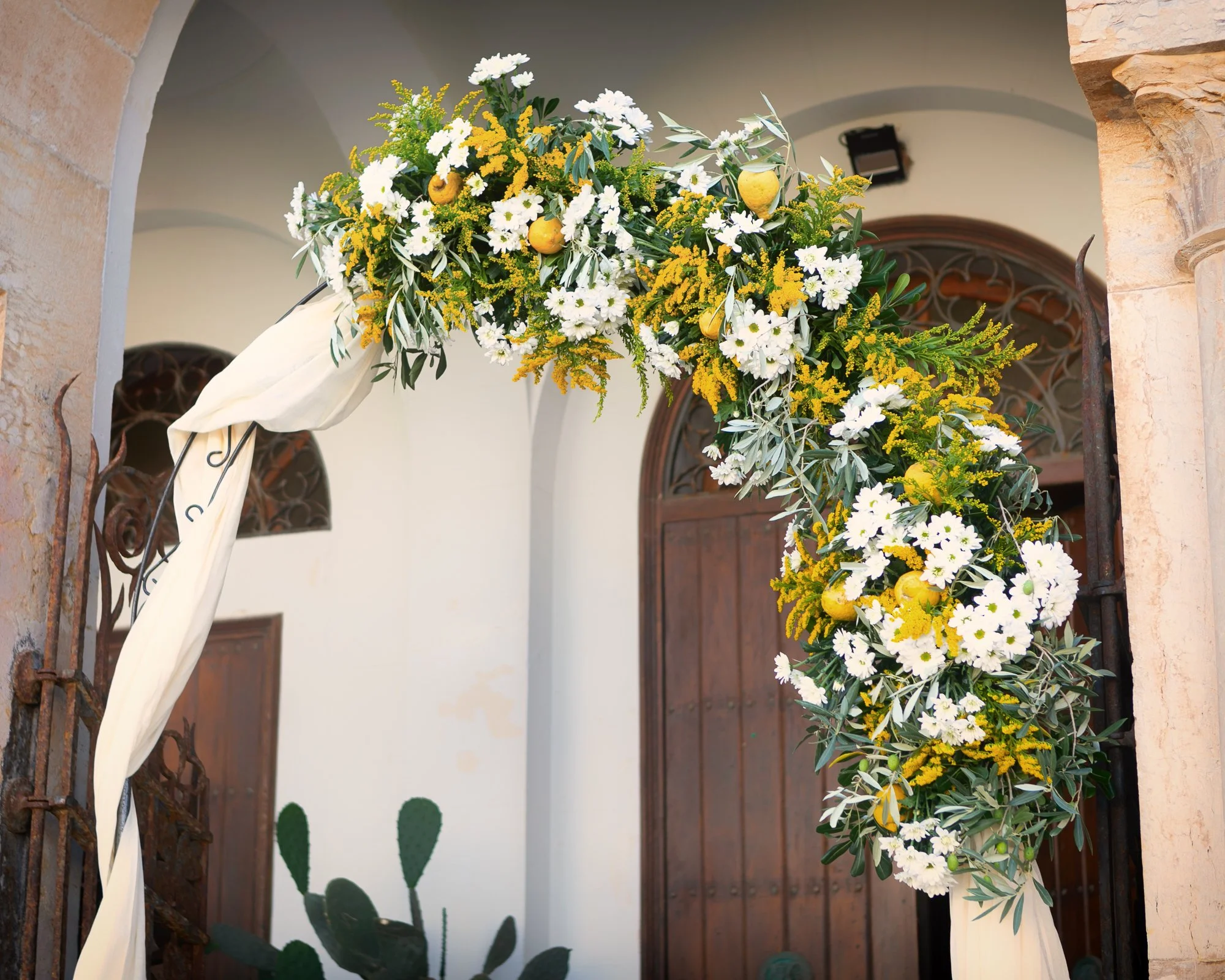 Mediterranean inspired wedding arch in Sicily featuring lemons, white flowers, olive branches, and floral styling by Alla Flora Giapponese.