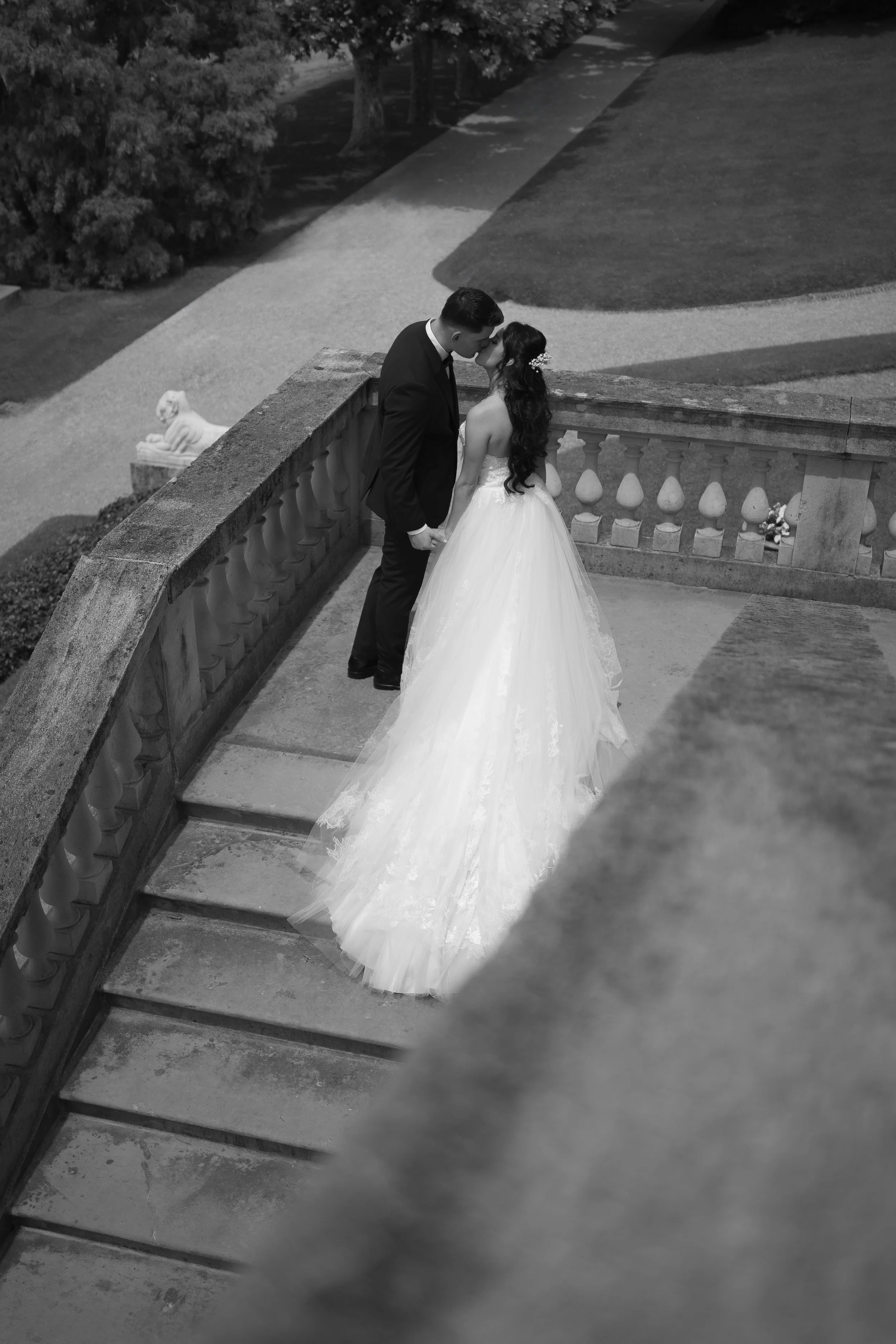 Black and white wedding portrait of a bride and groom sharing a kiss on a historic villa staircase.