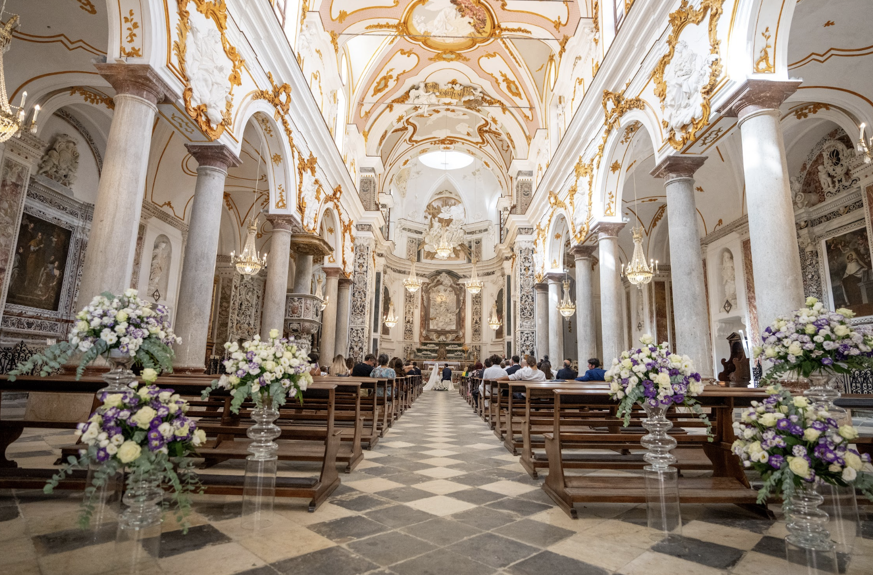 Luxury Italian church ceremony aisle decorated with large floral arrangements in white, purple, and green tones.
