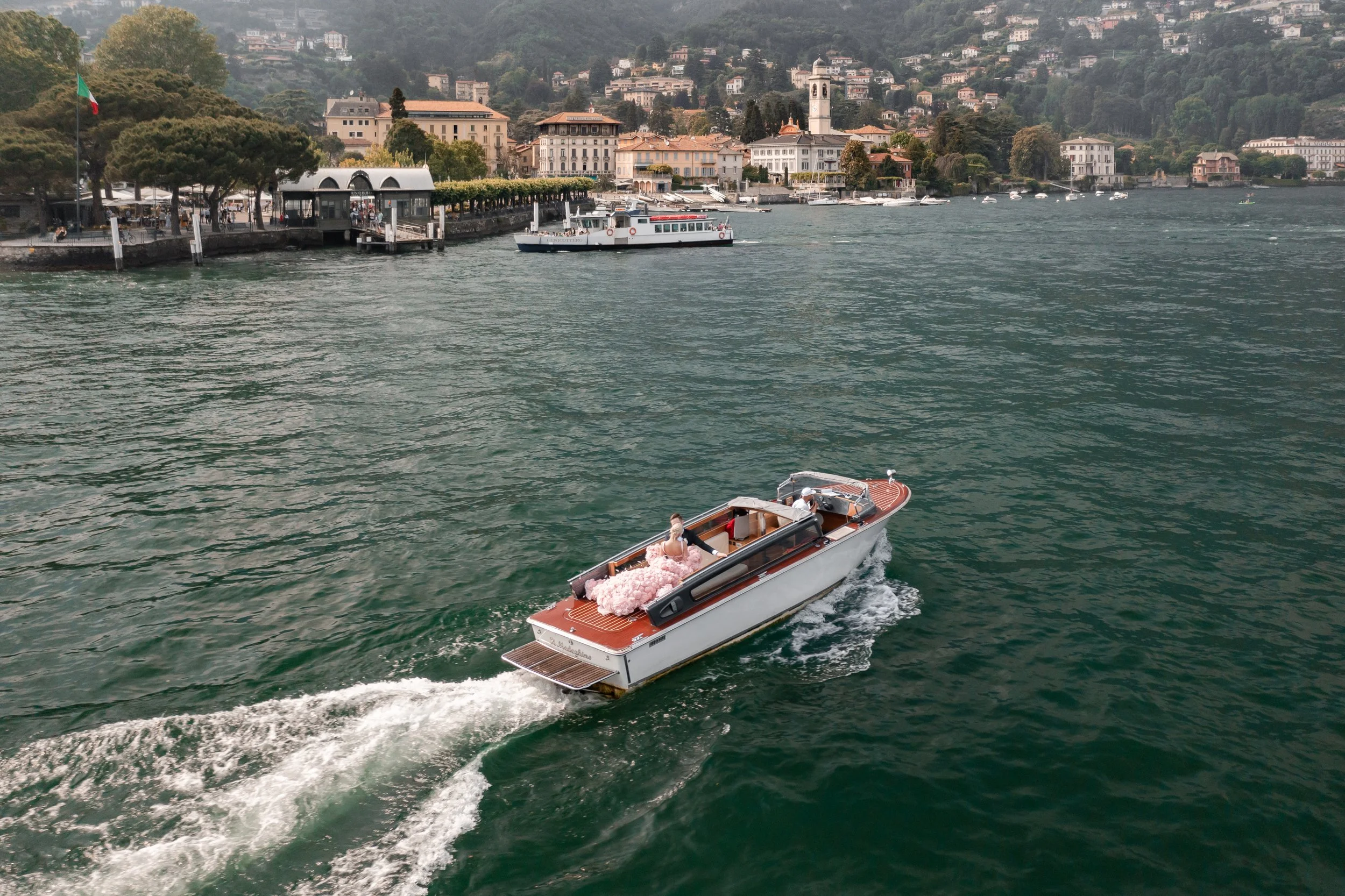 Aerial view of a bride travelling across Lake Como by classic wooden boat during her wedding celebration.