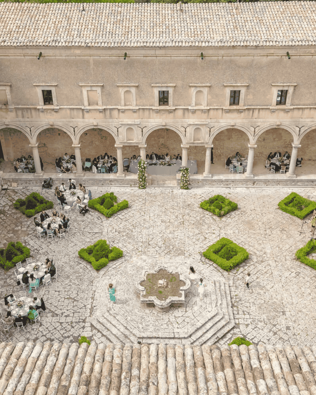 Aerial view of guests dining in the courtyard of a historic Sicilian monastery venue, surrounded by Renaissance arches and stone architecture during an Italian wedding reception.