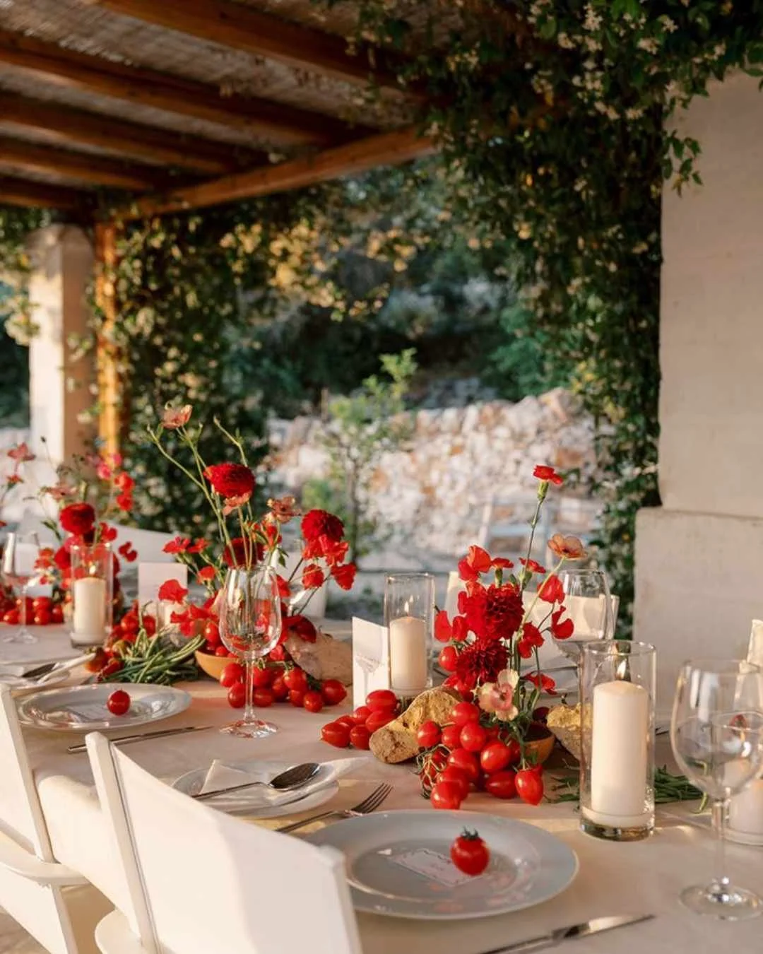 Bold red tomato and floral tablescape under a pergola in Puglia, showcasing Italy’s 2026 trend toward vibrant food-led décor.