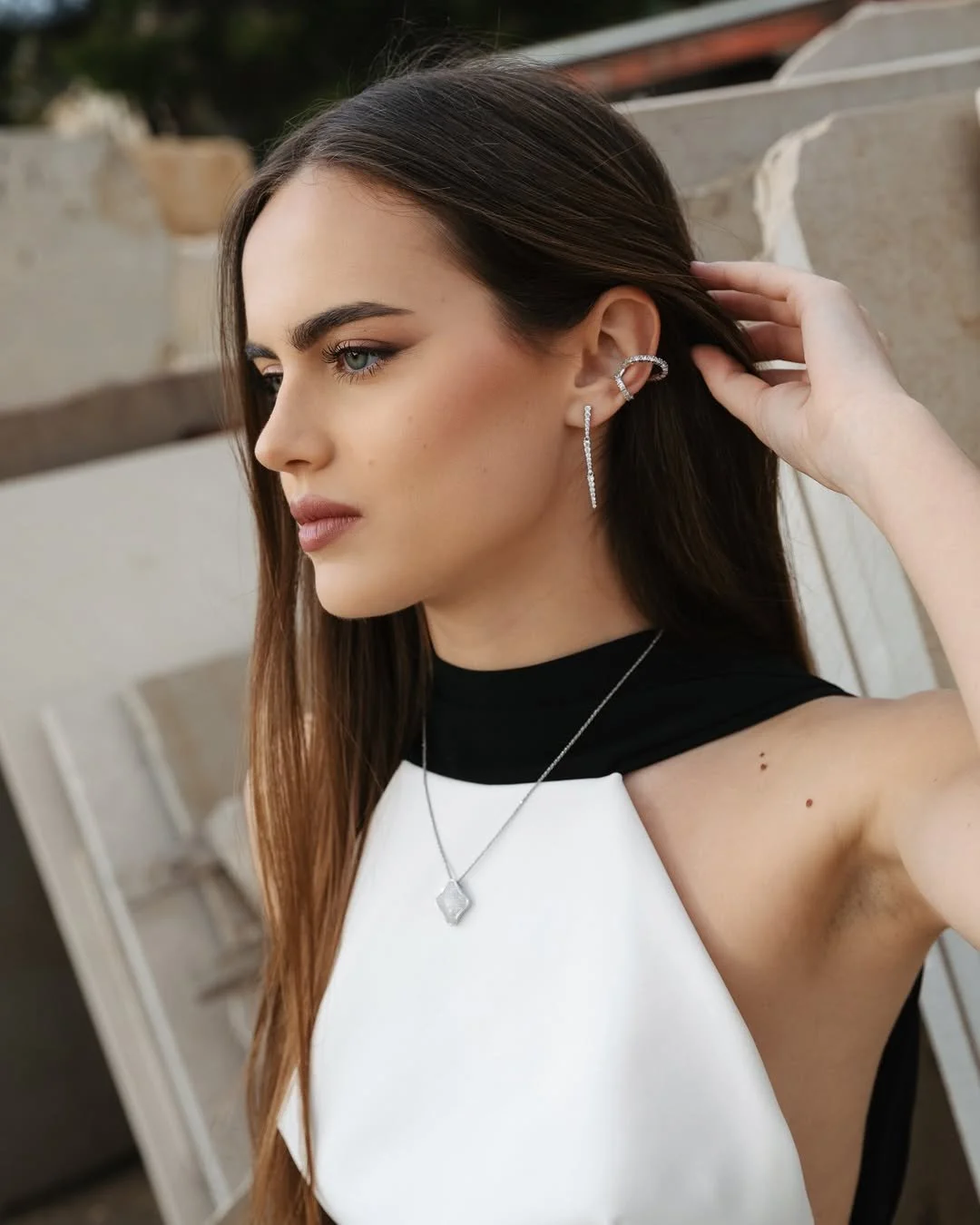 Portrait of a woman with long brunette hair, natural glam makeup, and elegant silver jewellery wearing a black and white outfit.”