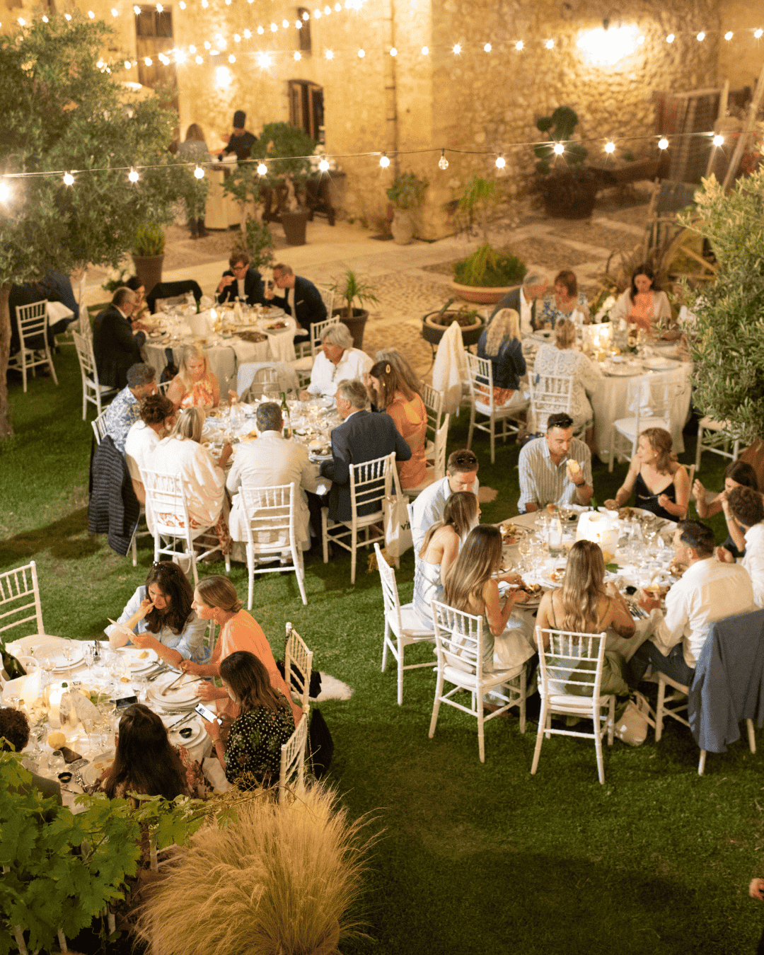 Outdoor wedding reception in Italy with guests dining under string lights in a rustic courtyard, showing a realistic Italy wedding setup and budget style
