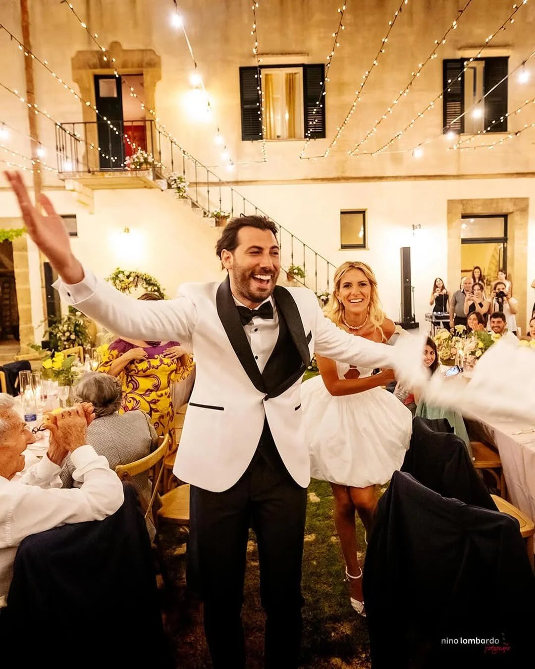 Bride and groom entering their wedding reception with guests under warm string lights in Sicily