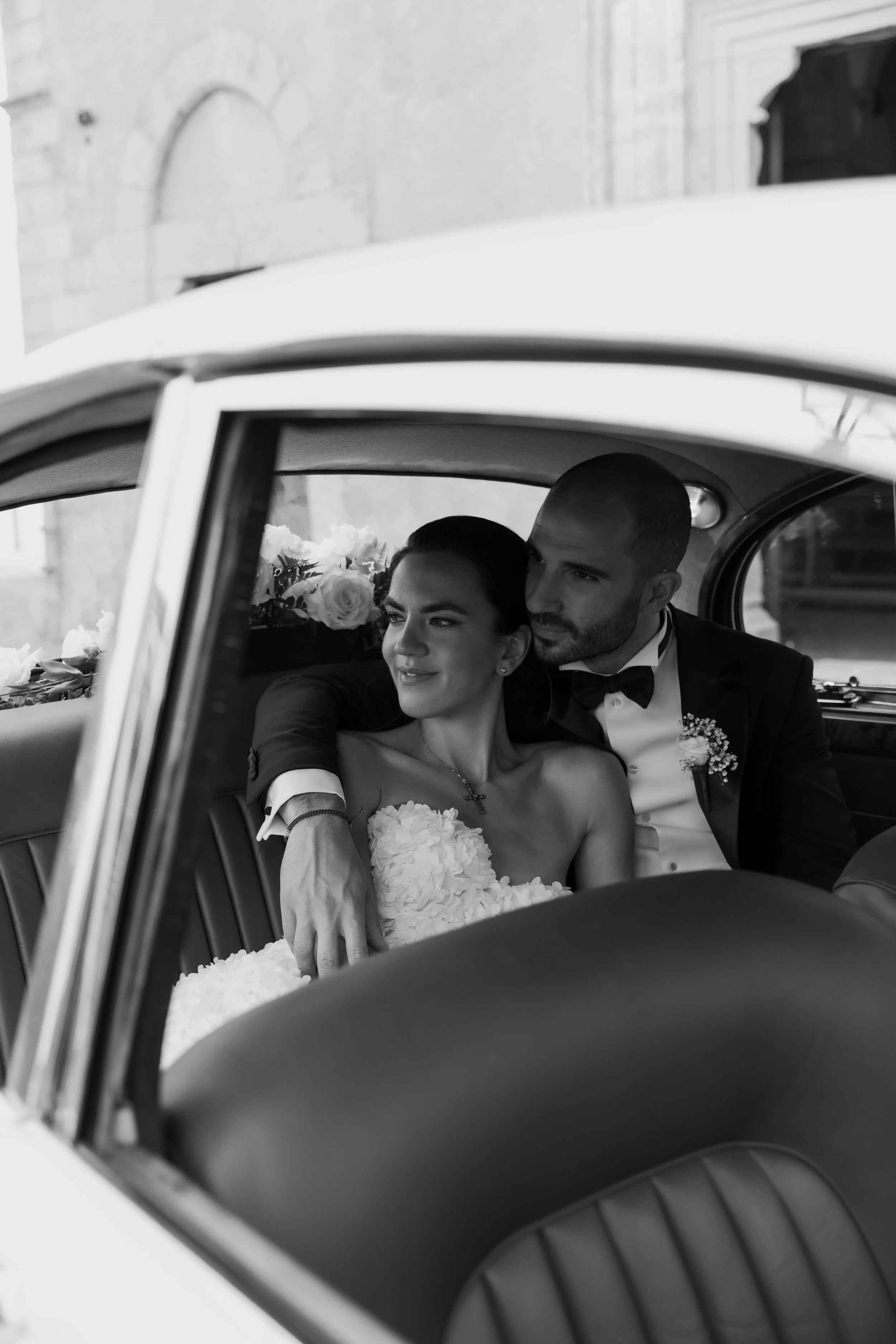 Bride and groom seated together inside a vintage wedding car in Italy, photographed in black and white by Lauren Young.