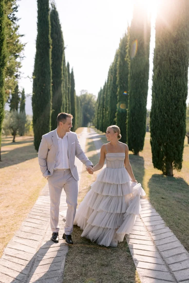 Couple walking hand in hand along a cypress lined path in Tuscany after their wedding ceremony.