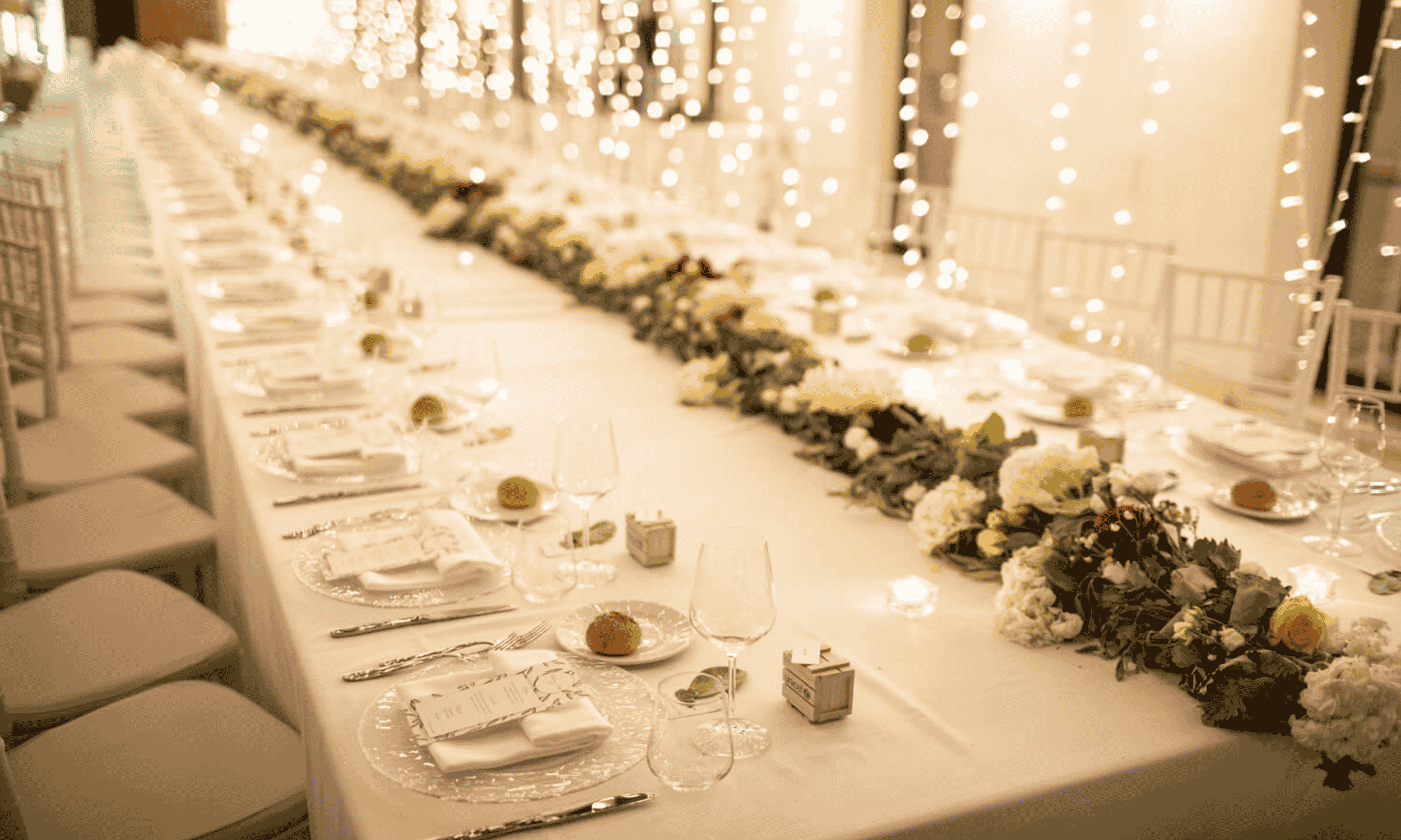 Elegant long wedding reception table in Italy with floral garland, candles and warm fairy lights creating a romantic indoor setting
