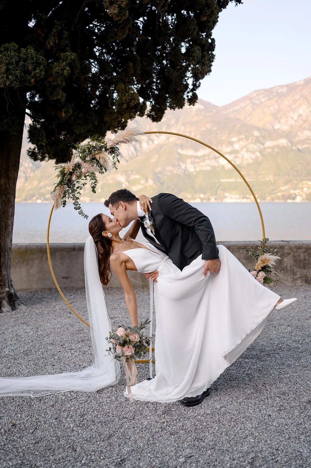 Bride and groom sharing a kiss during a romantic lakeside elopement ceremony at Lake Como, Italy, with mountain views and a floral ceremony arch.