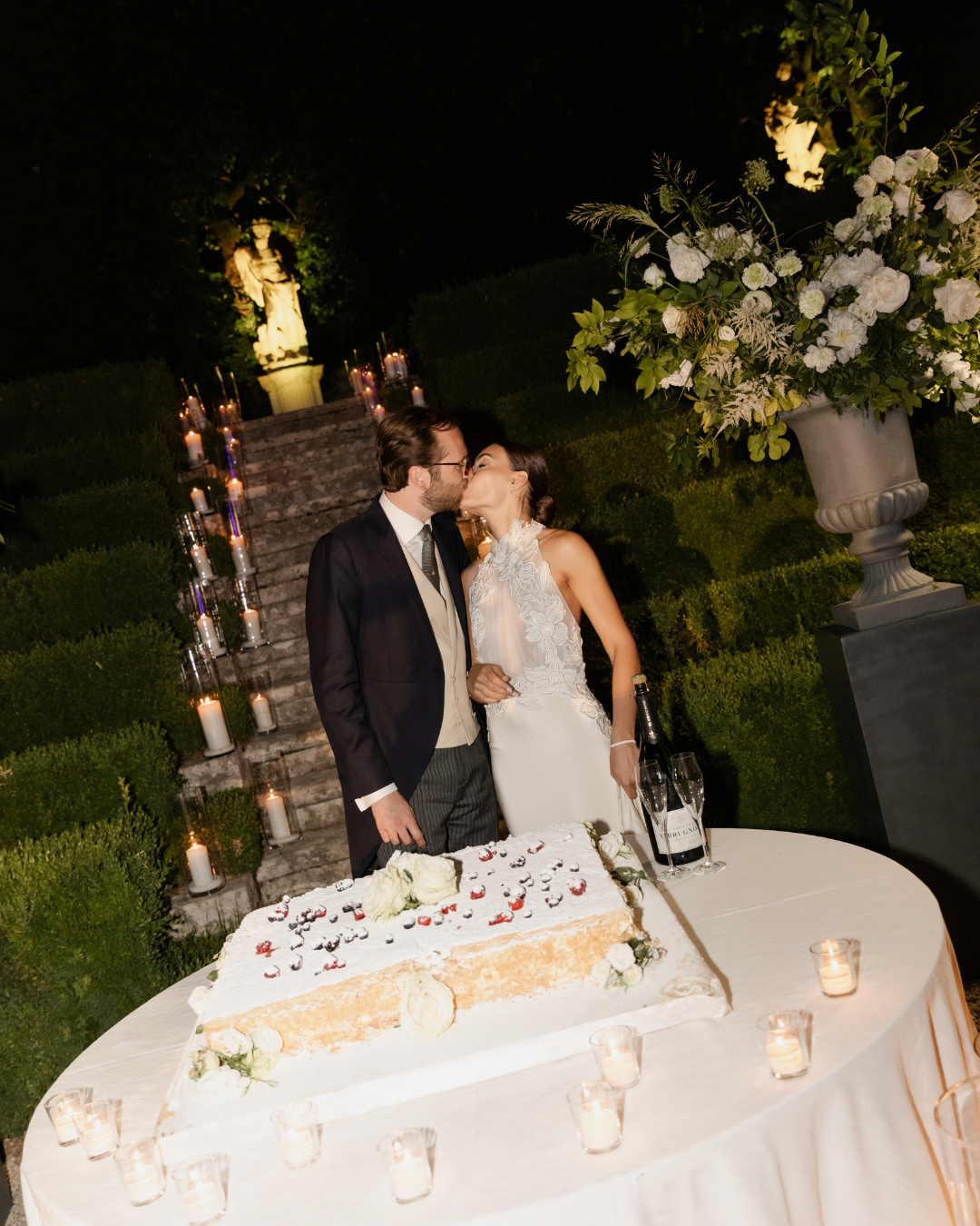 Newlyweds kissing beside their wedding cake during an elegant evening reception in Italy, photographed by Lauren Young.