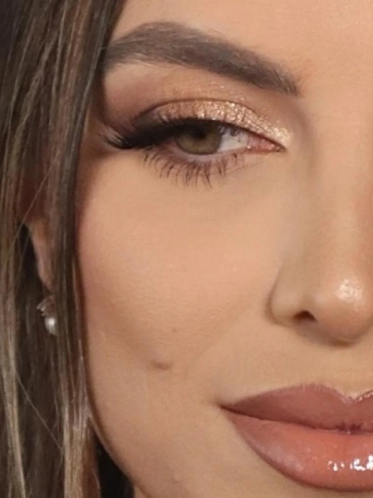 Close-up of soft glam makeup featuring gold shimmer eyeshadow, long lashes, defined brows, and glossy nude lips.