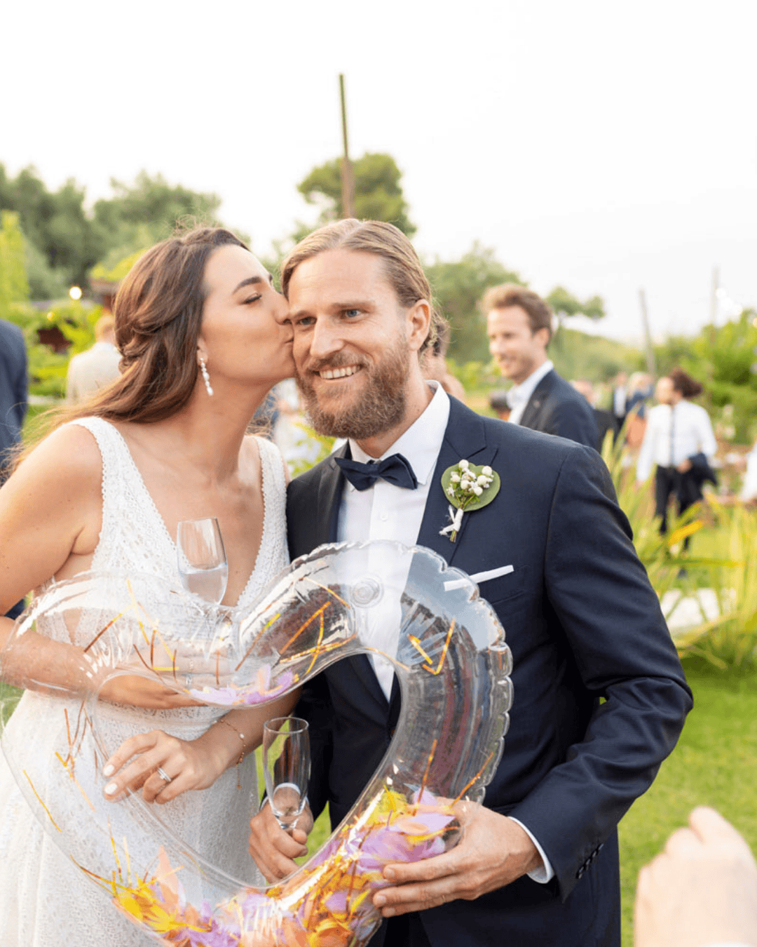 Bride kissing groom during outdoor wedding aperitivo in Italy with guests and garden setting
