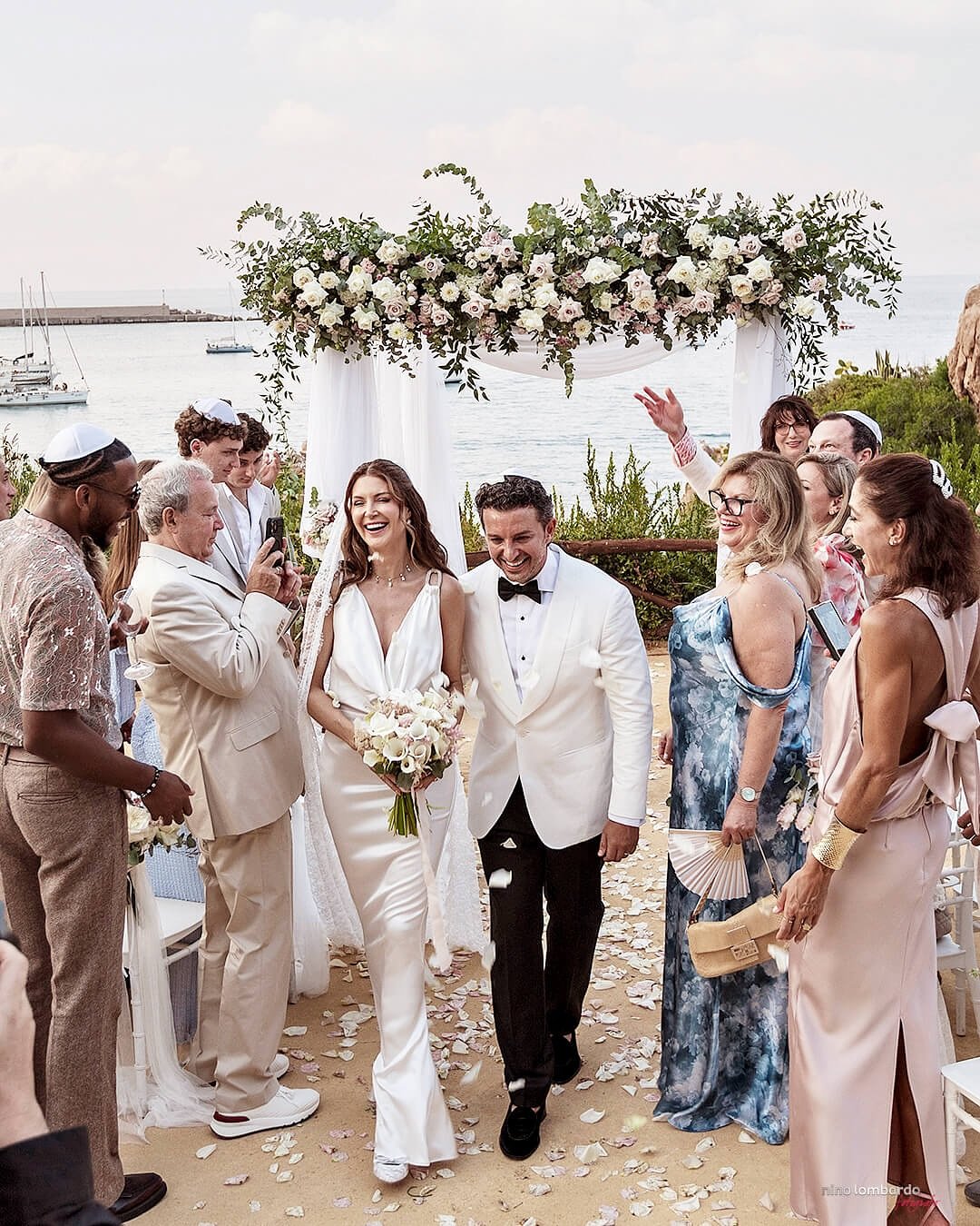 Bride and groom walking down the aisle after a seaside wedding ceremony in Sicily with floral arch and guests