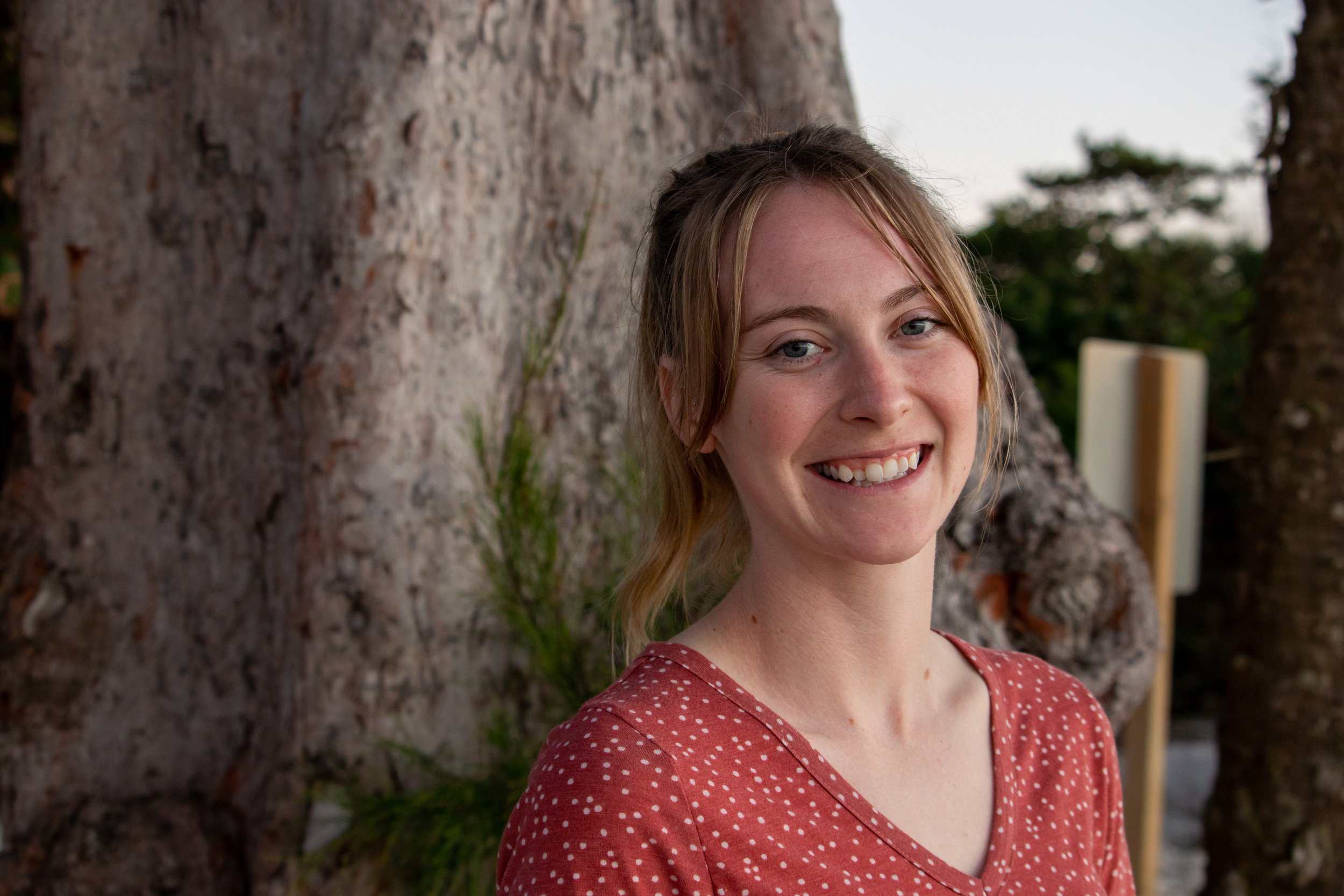 Smiling woman standing outdoors in front of a large tree.