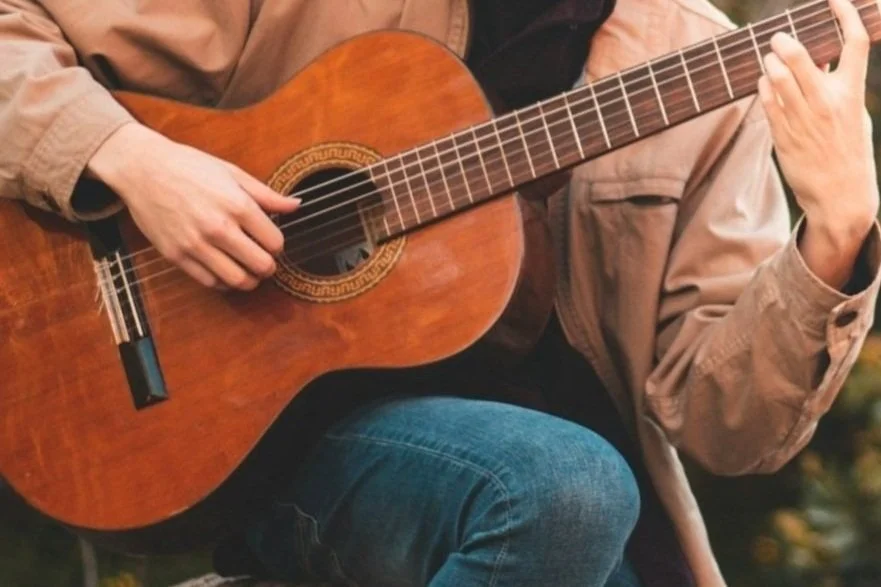 Person playing an acoustic guitar in an outdoor setting.