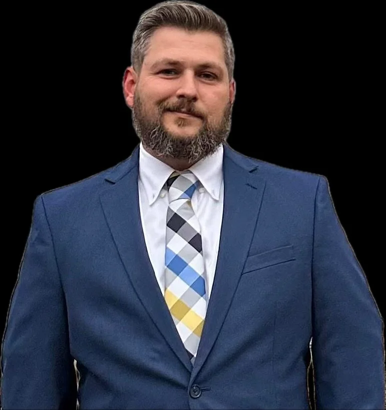 Man in a blue suit with a multicolored plaid tie standing against a black background.